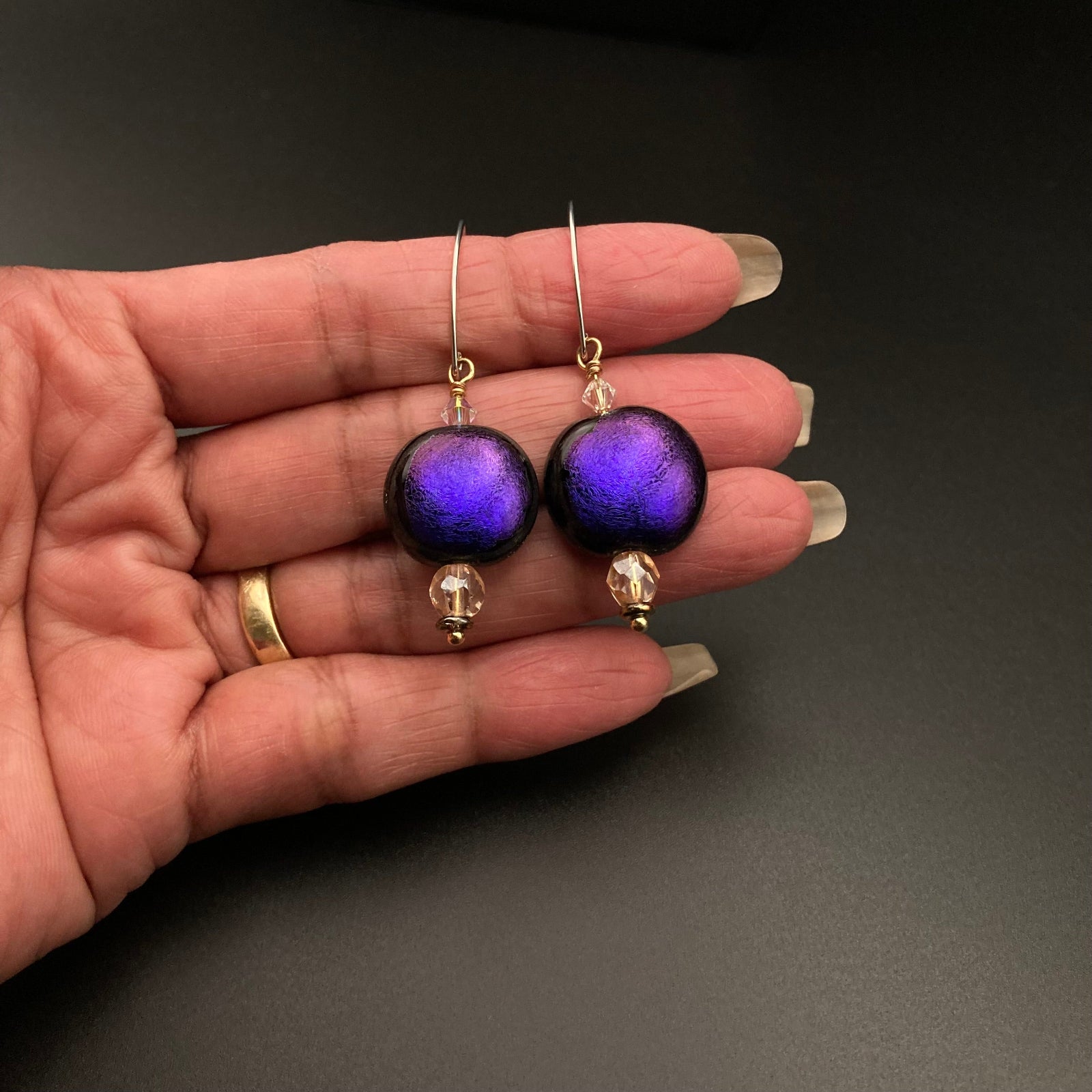 Hand holding handmade purple glass earrings, by 3D Glass Designs.