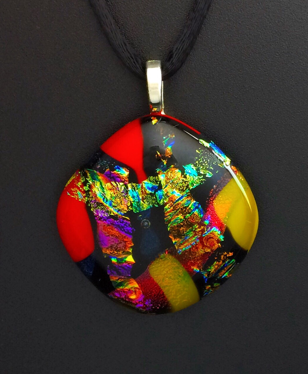 Colorful dichroic fused glass pendant in red, blue, yellow, purple, green and gold colors with a black satin cord. By 3D Glass Designs.