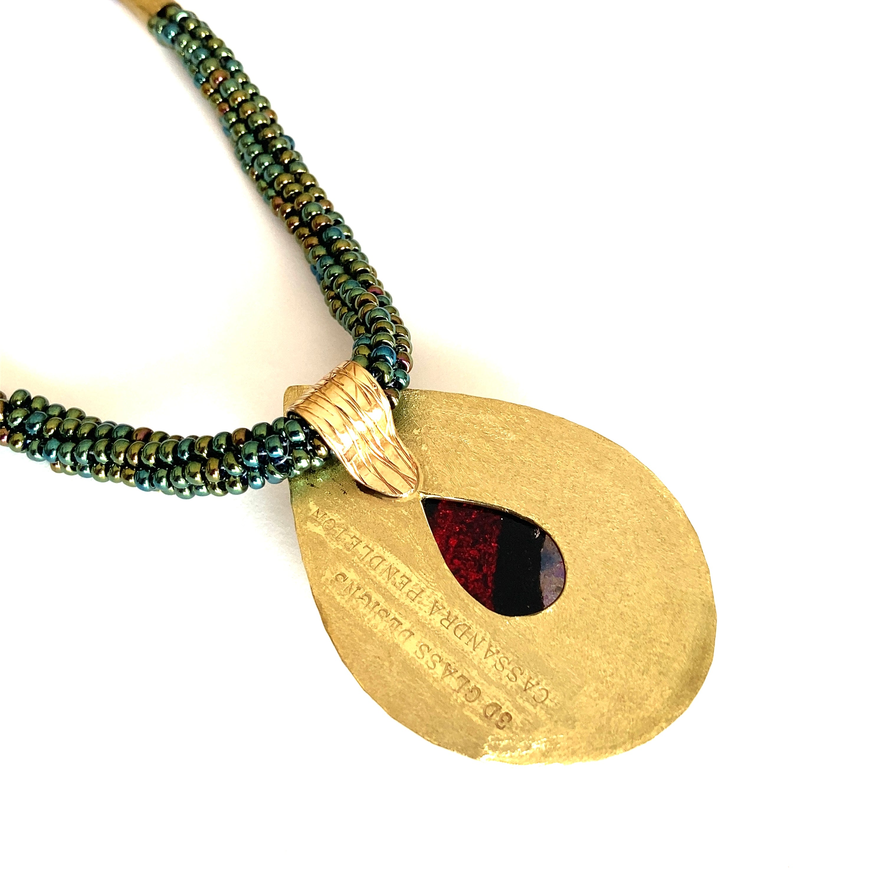 The back of teardrop shaped brass and dichroic glass pendant necklace with a beaded necklace.