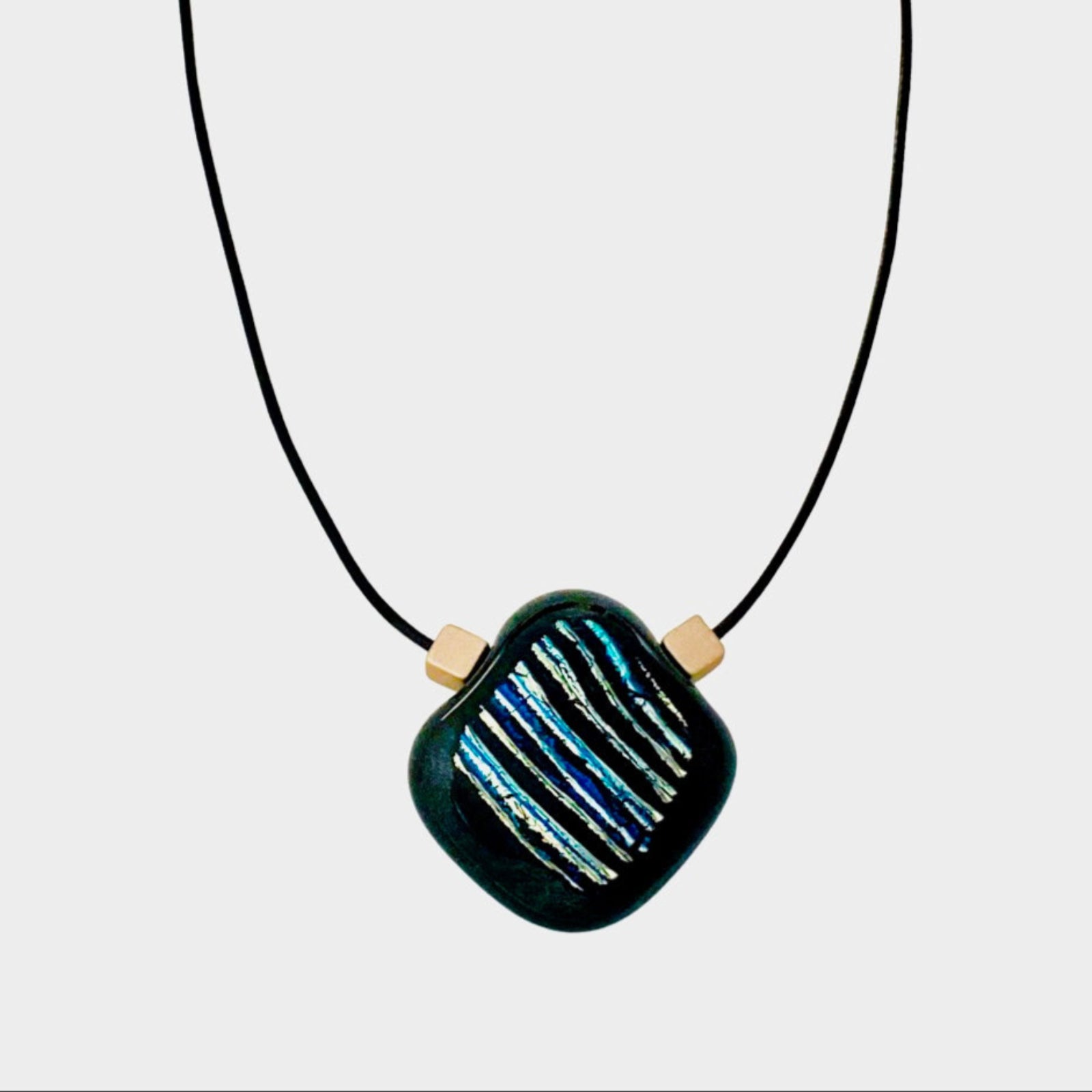 Blue striped dichroic glass pendant with gold cube beads on a leather cord against a white background, by 3D Glass Designs.
