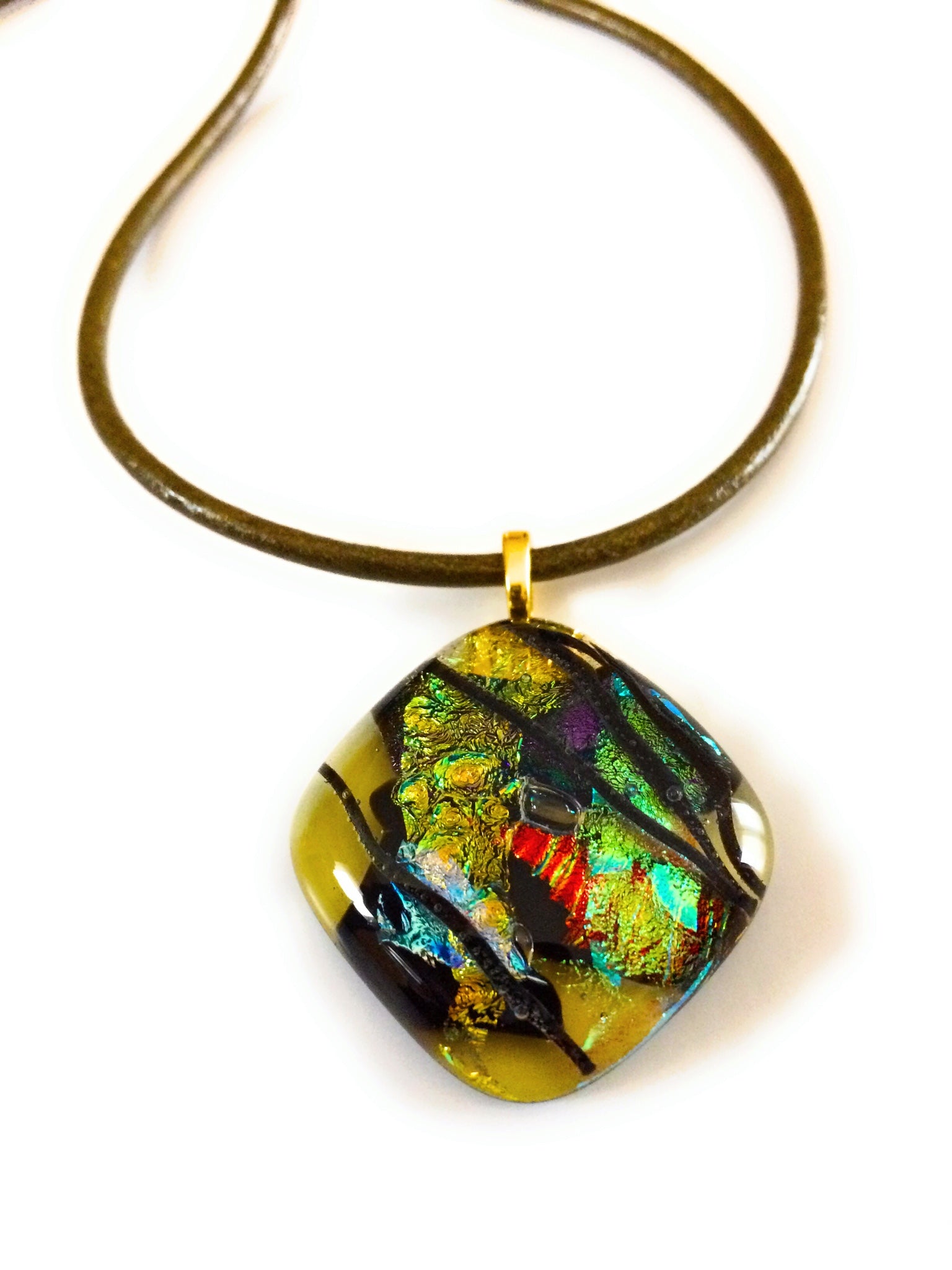 Fused glass pendant in transparent yellow with red, blue, green, purple and gold dichroic glass. Streaks of black add contrast to the design. Diamond shaped pendant hangs on an olive-green leather cord, by 3D Glass Designs.