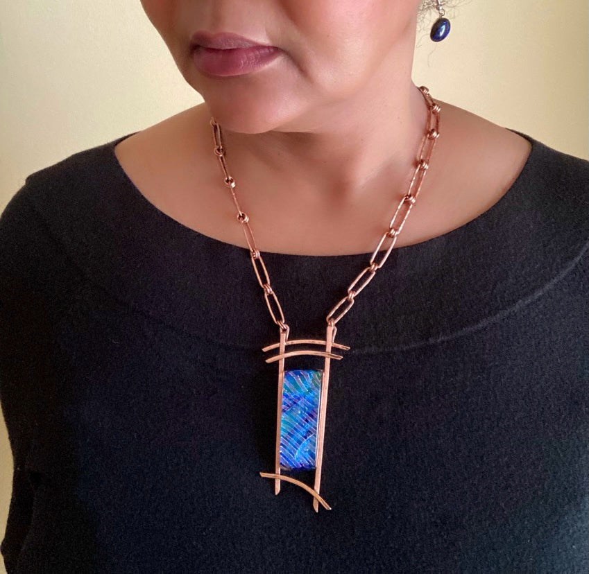 Model wearing blue dichroic glass set in handcrafted copper pendant with an Asian design. Handmade copper paperclip link chain completes the design, by 3D Glass Designs