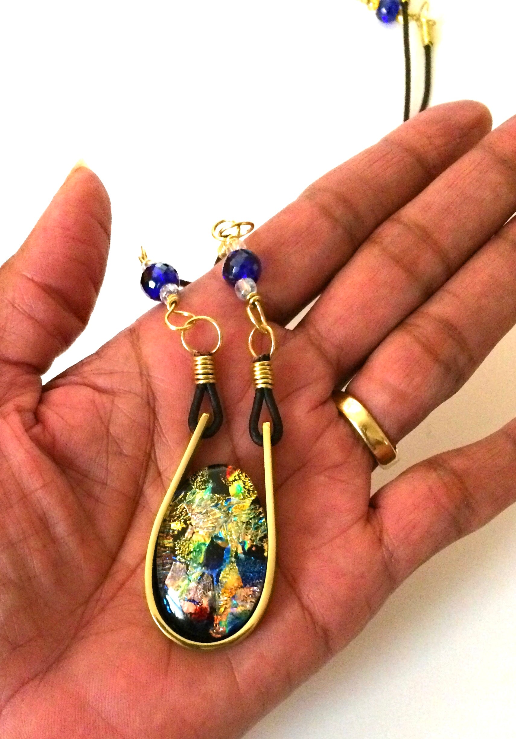Hand holding modern fused dichroic glass and brass pendant with a beaded leather cord, by 3D Glass Designs.