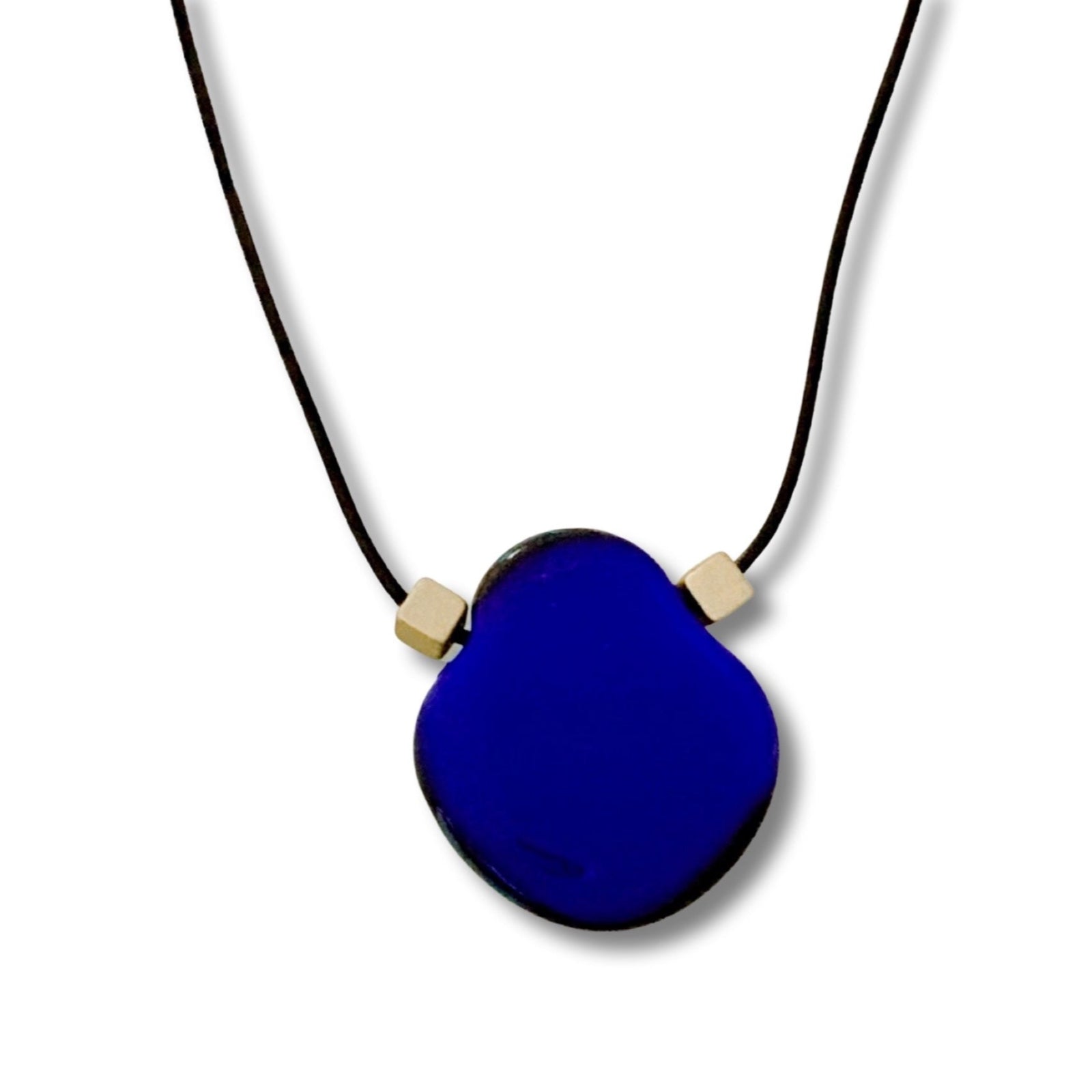 Vibrant blue fused glass pendant on a leather cord against a white background.
