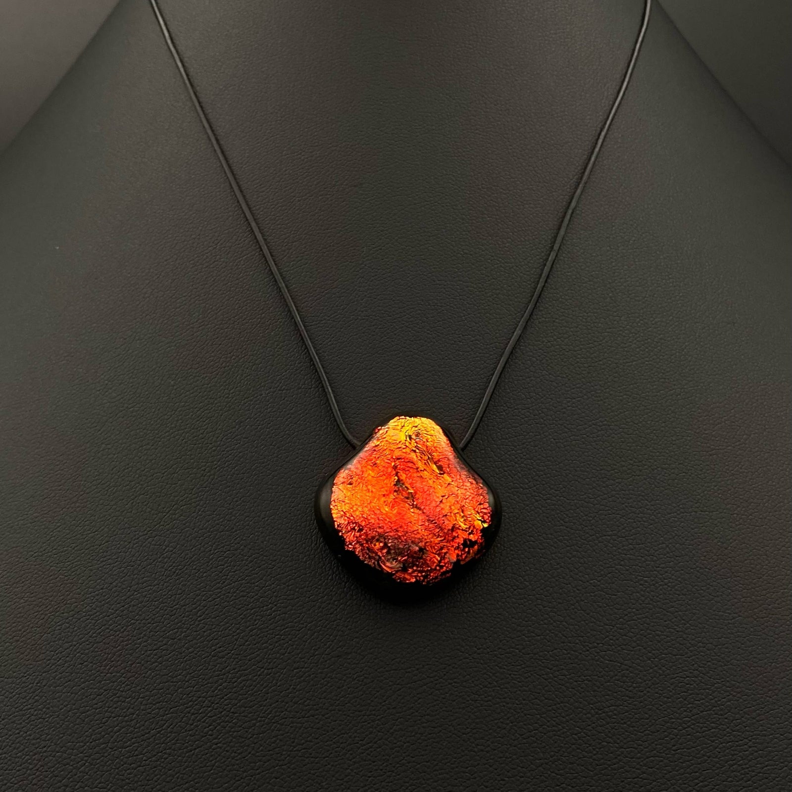 Red dichroic glass pendant with black leather necklace on a black background, by 3D Glass Desins.