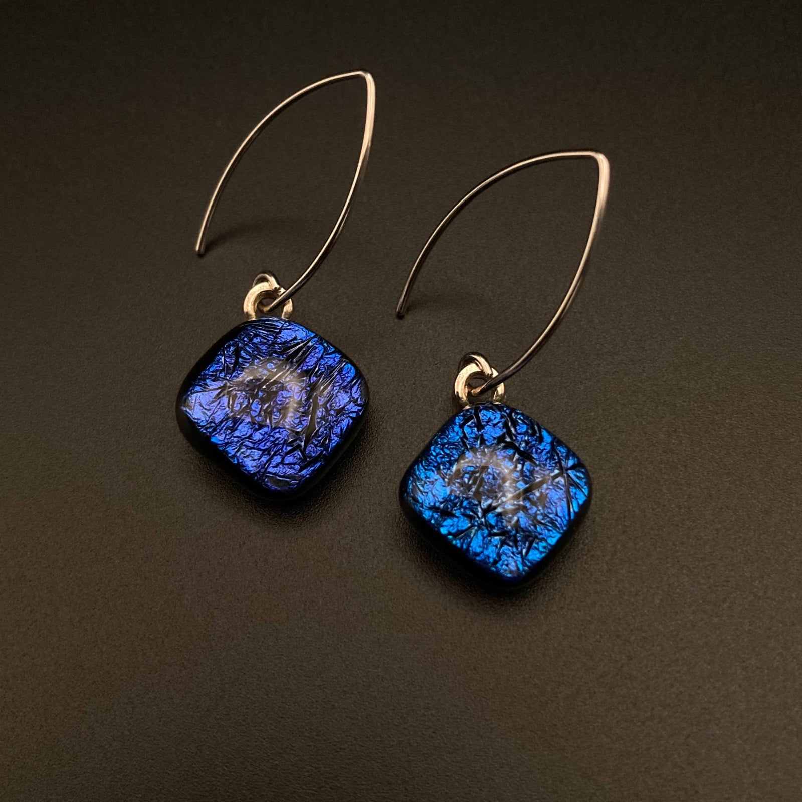 A pair of diamond-shaped glass dangle earrings with silver ear wires against a grey background, by 3D Glass Designs.