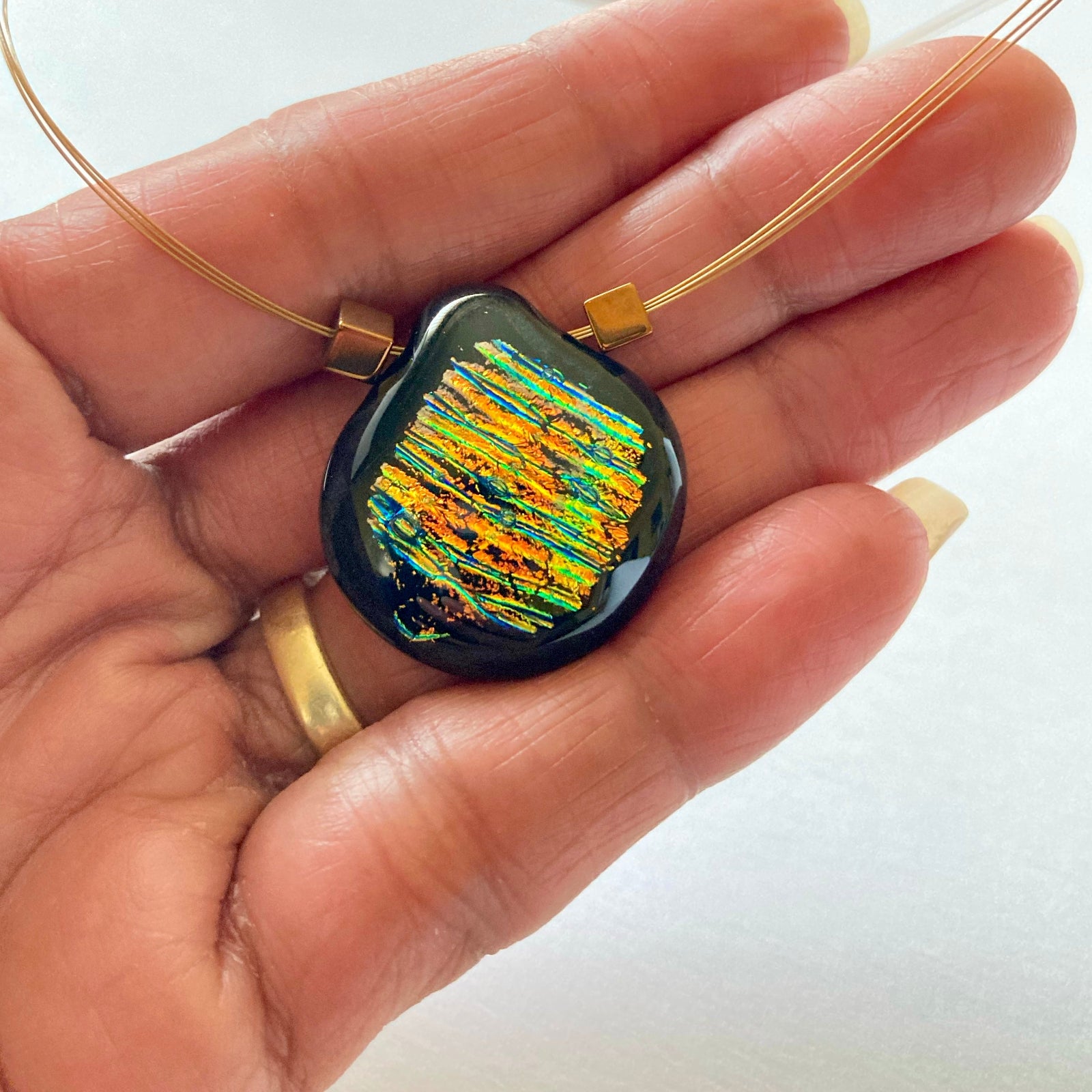 Hand holding dichroic glass pendant, by 3D Glass designs.