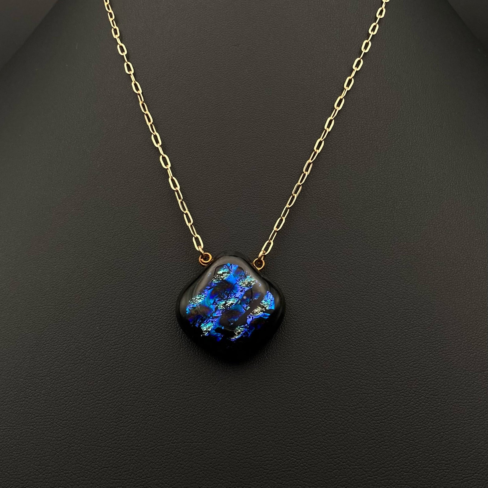 Pear-shaped glass pendant on a gold chain against a black background, by 3D Glass Designs.