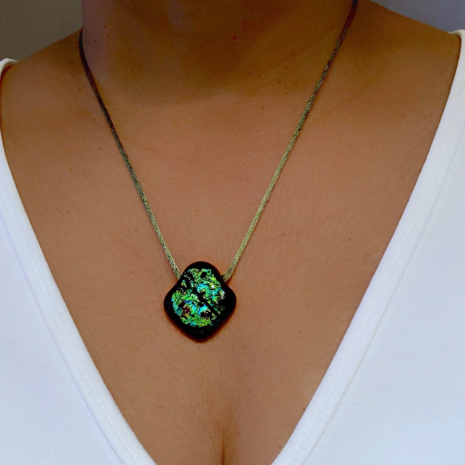 Model wearing white shirt and green glass pendant on an olive-green satin cord, by 3D Glass Designs.
