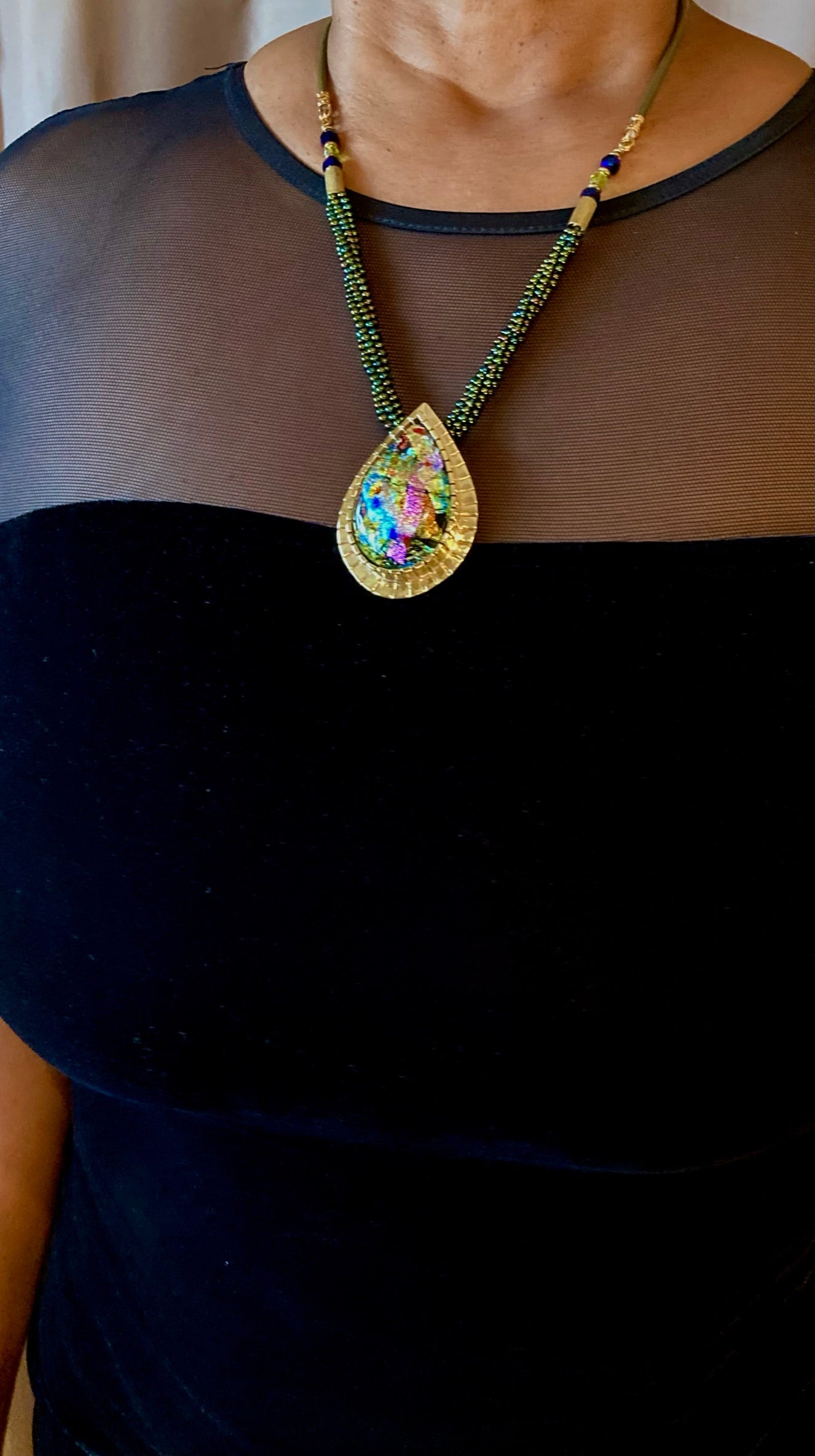 Model wearing black evening dress with handcrafted dichroic glass and brass pendant with beaded necklace. By 3D Glass Designs.