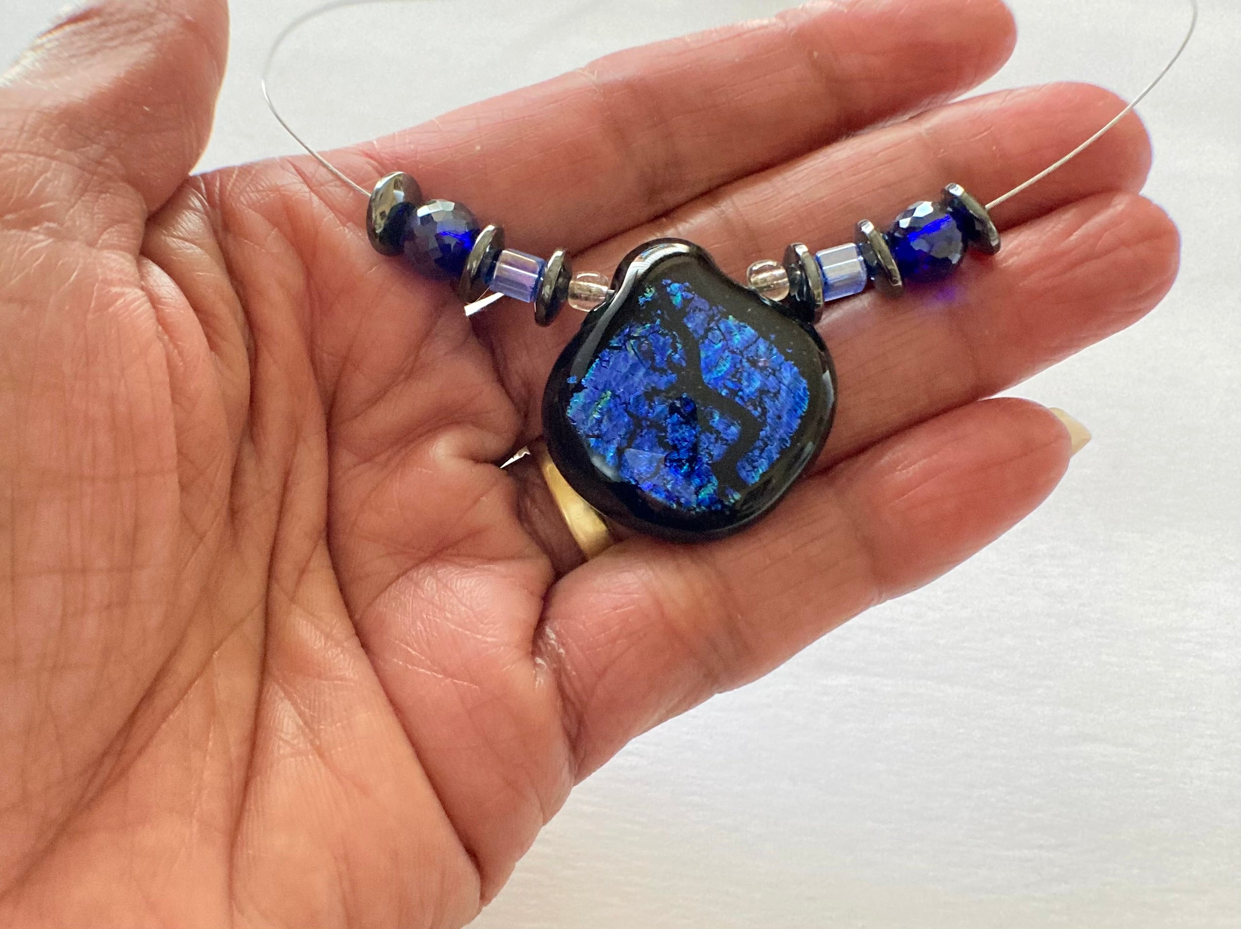 Model's hand holding handmade beaded necklace against a white background, by 3D Glass Designs.