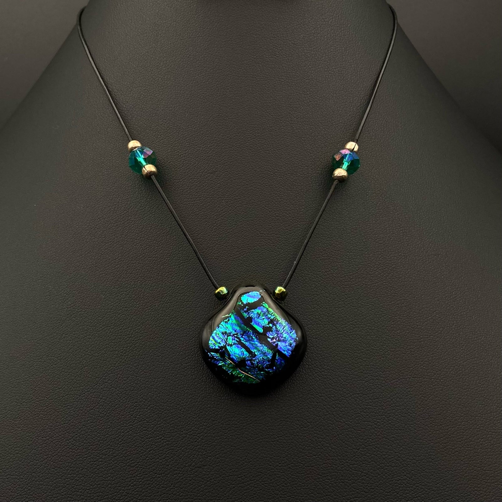 Blue-green glass pendant on a beaded black leather cord against a black background, by 3D Glass Designs.