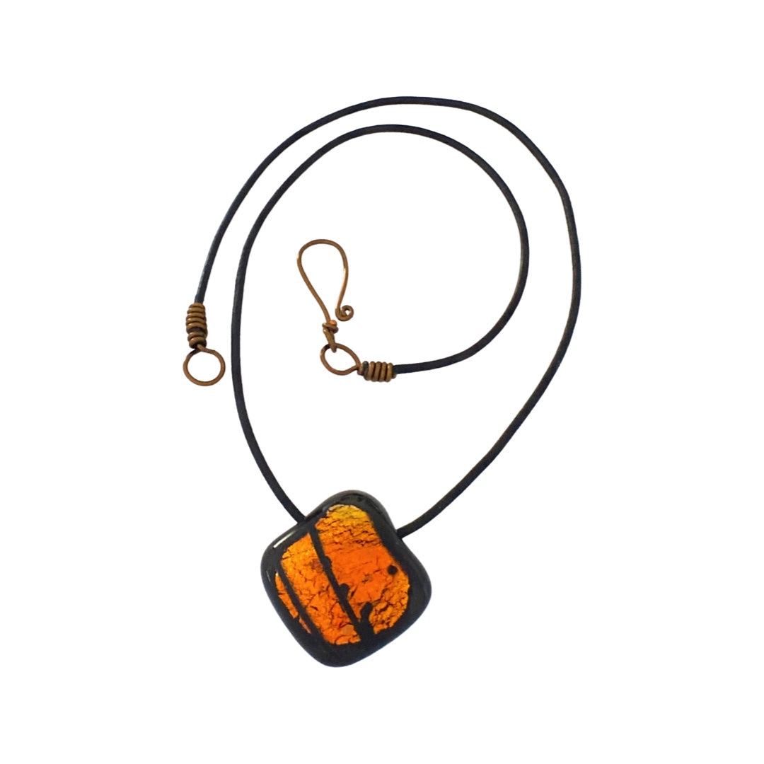 Orange and black fused glass pendant on a black leather cord against a white background, by 3D Glass Designs.