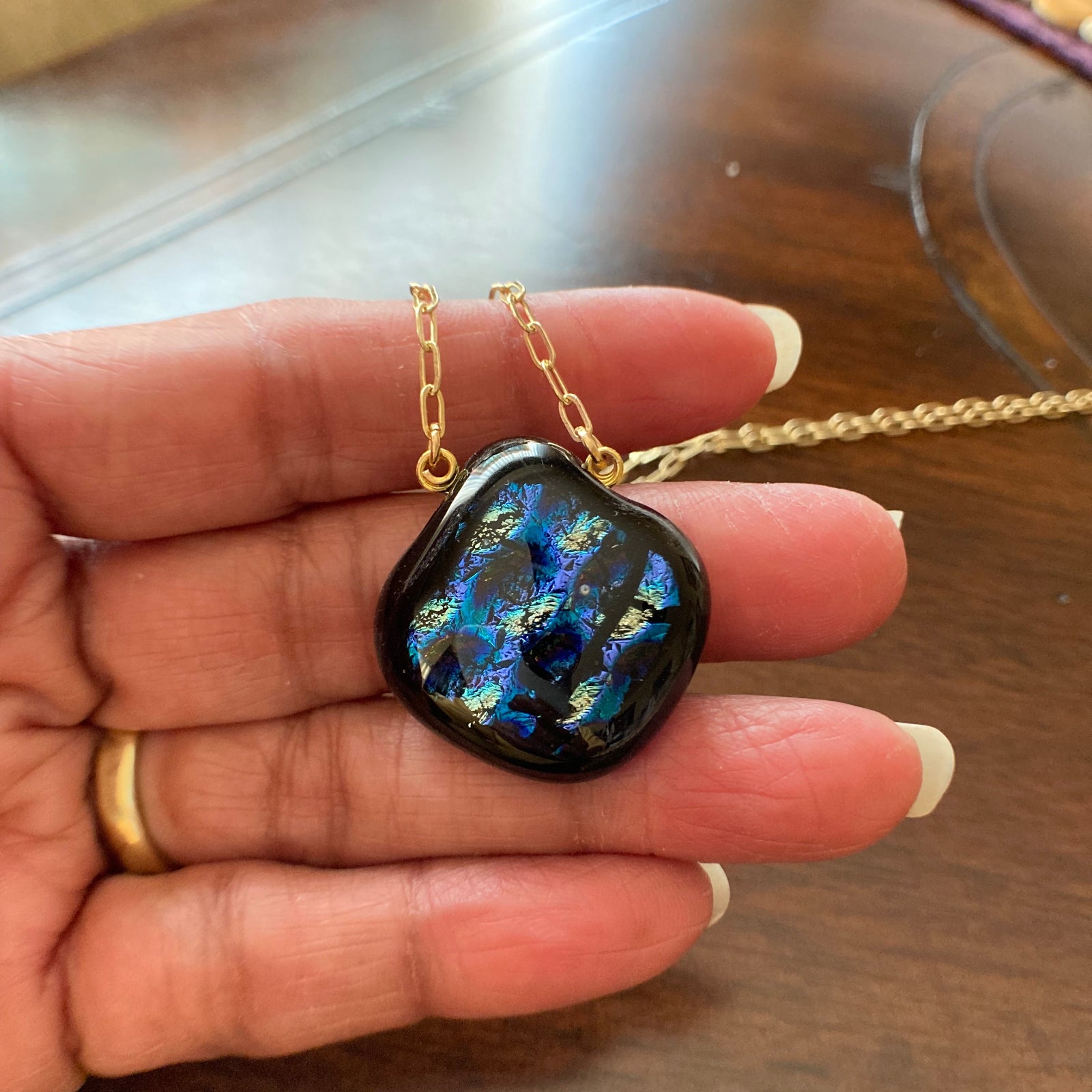 Hand holding pear-shaped glass pendant against a wooden table, by 3D Glass Designs