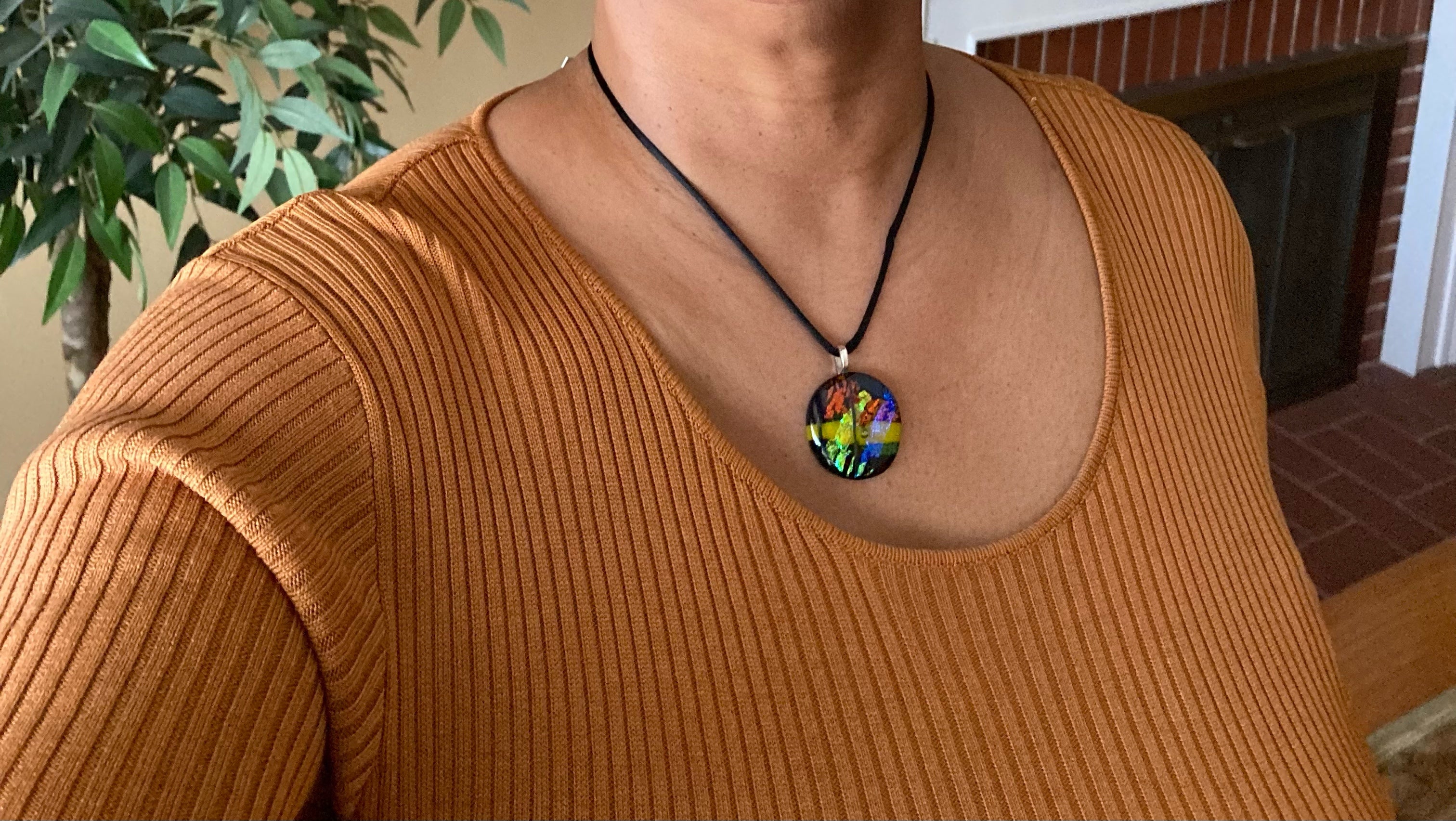 Model wearing multicolor fused glass pendant in a Livingroom, by 3D Glass Designs.