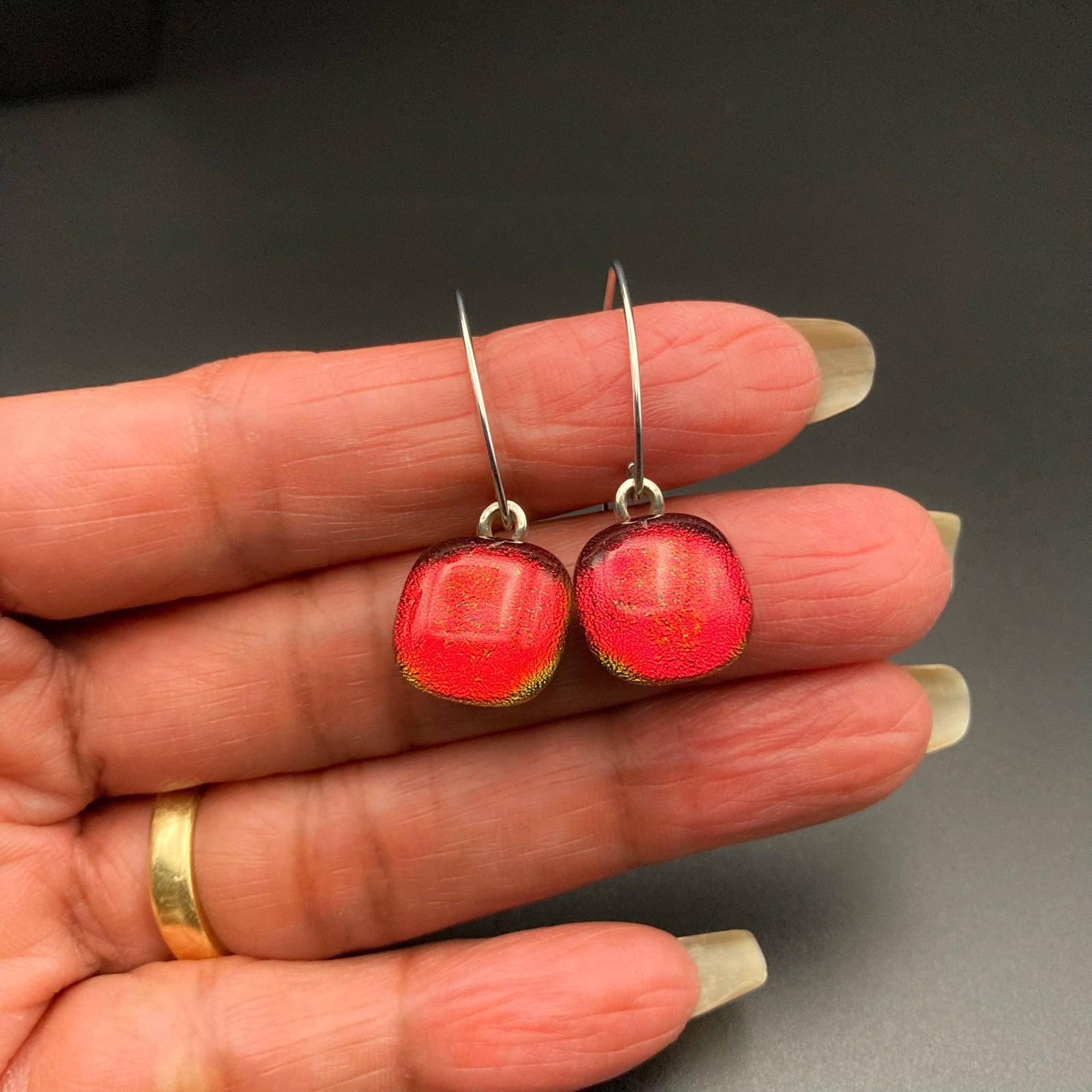 Hand holding a pair of red glass pierced earrings, by 3D lass Designs.