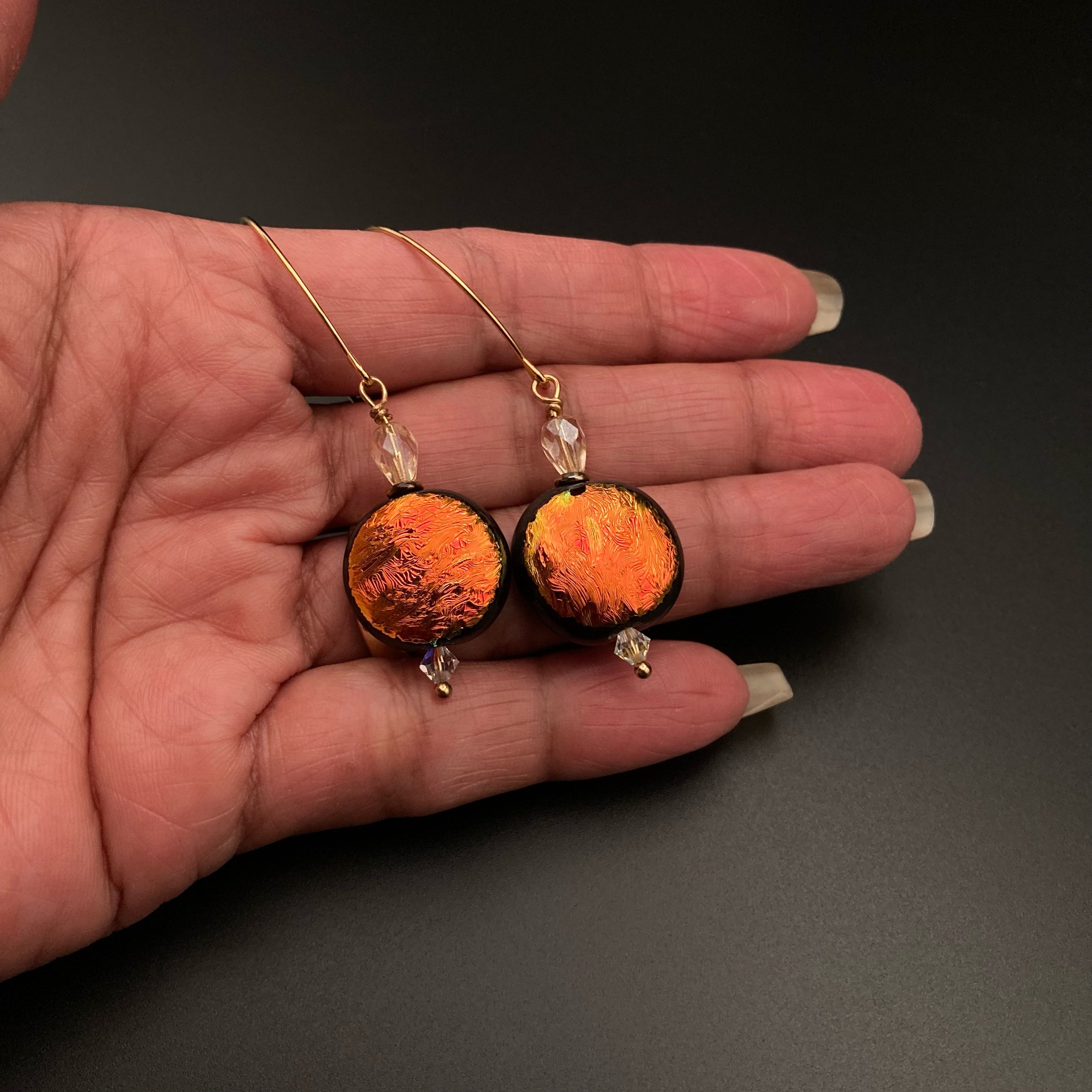 Hand holding orange fused glass earrings, by 3D Glass Designs.