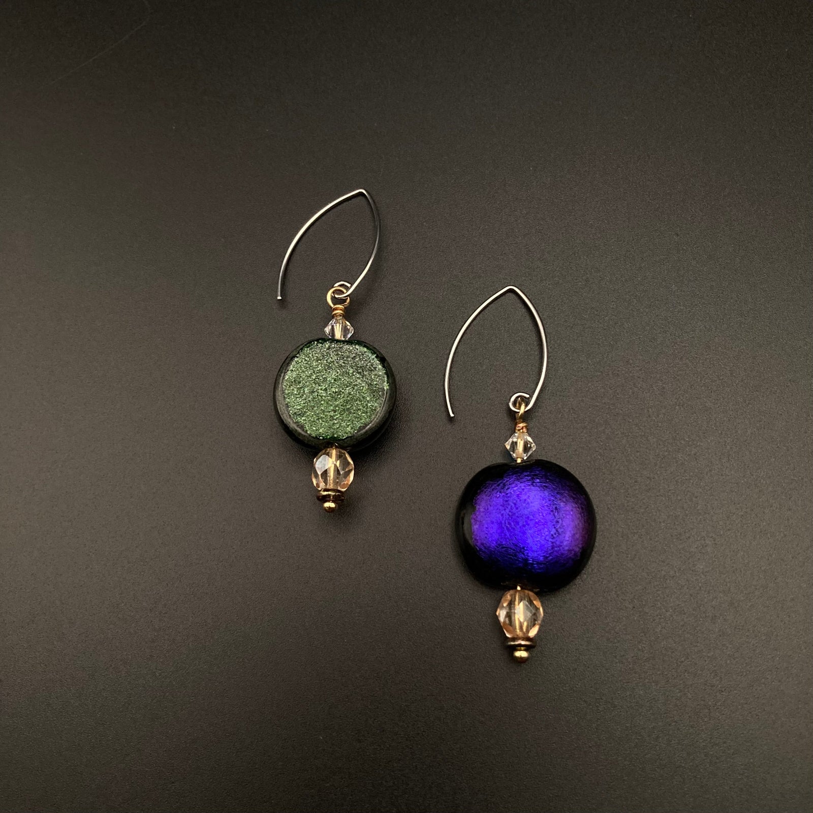 A pair of reversible glass earrings with one side green and the other purple glass, by 3D Glass Designs.