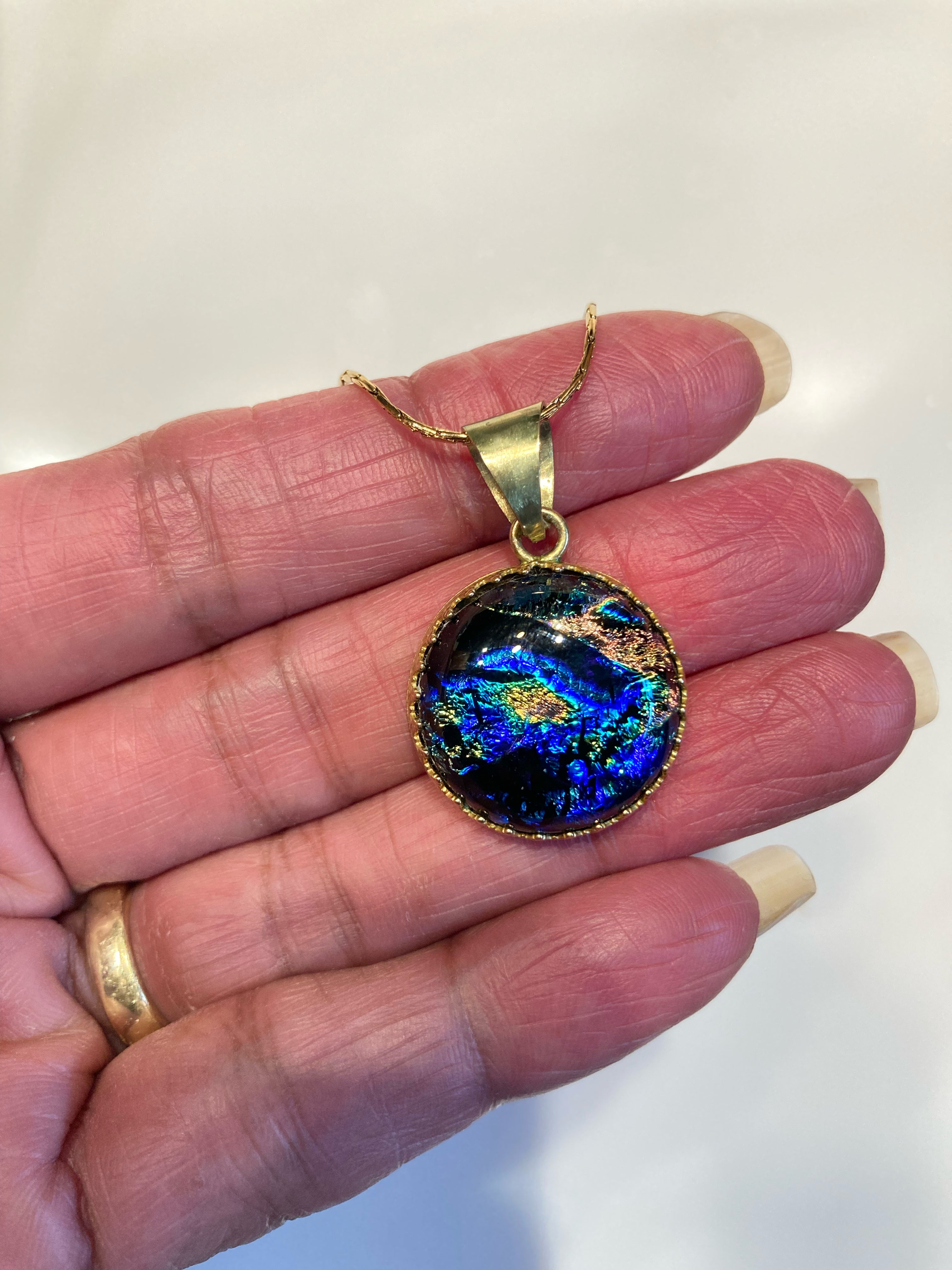 Models hand holding small dichroic glass and brass pendant. By 3D Glass Designs.