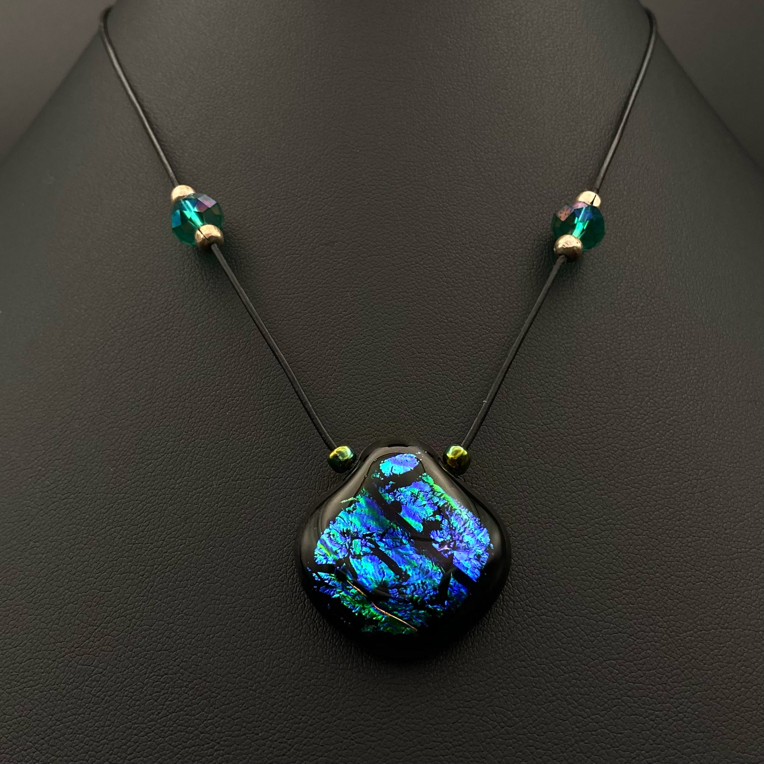 Blue-green glass pendant on a beaded black leather cord against a black background, by 3D Glass Designs.