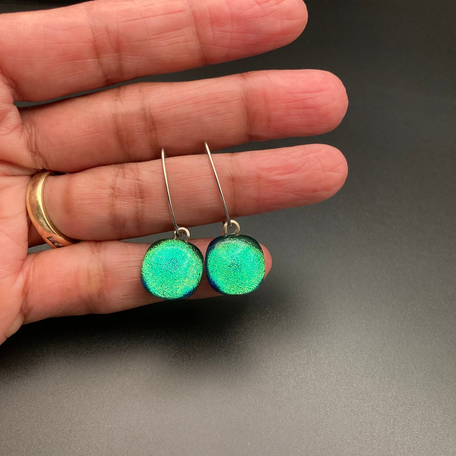 Hand holding a pair of pierced earrings with teal-green glass drops, by 3D Glass Designs.