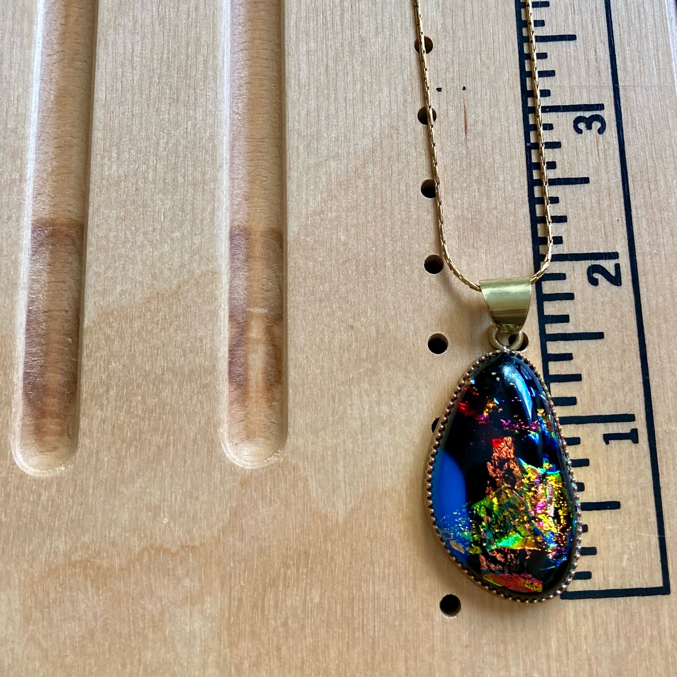 Small dichroic pendant shown on a wooden measuring board. By 3D Glass Designs.