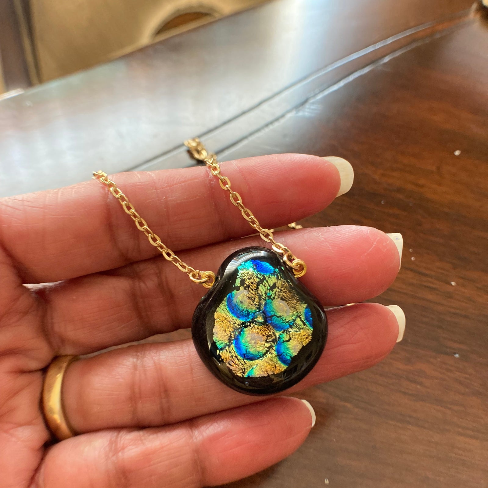 Hand holding fused glass pendant against a wooden table, by 3D Glass Designs.