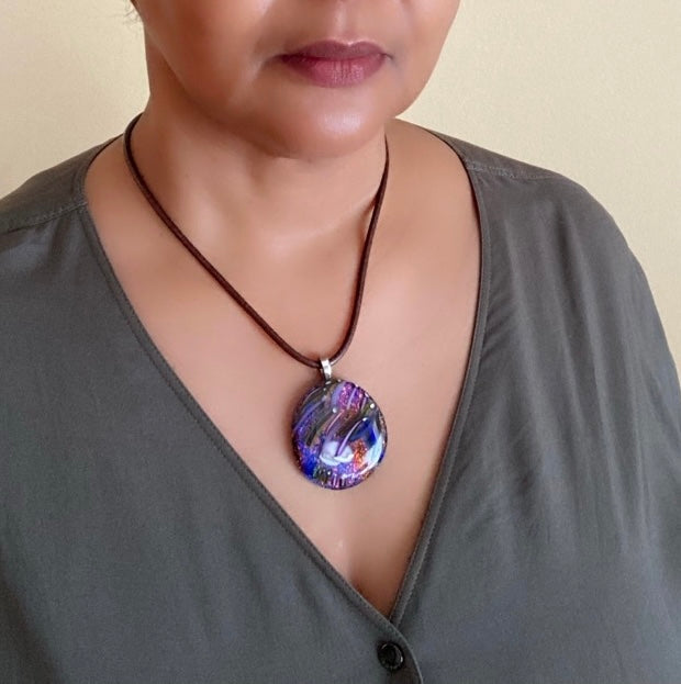 Model wearing large, round dichroic glass pendant with handblown glass detail that resembles shooting stars. By 3D Glass Designs.