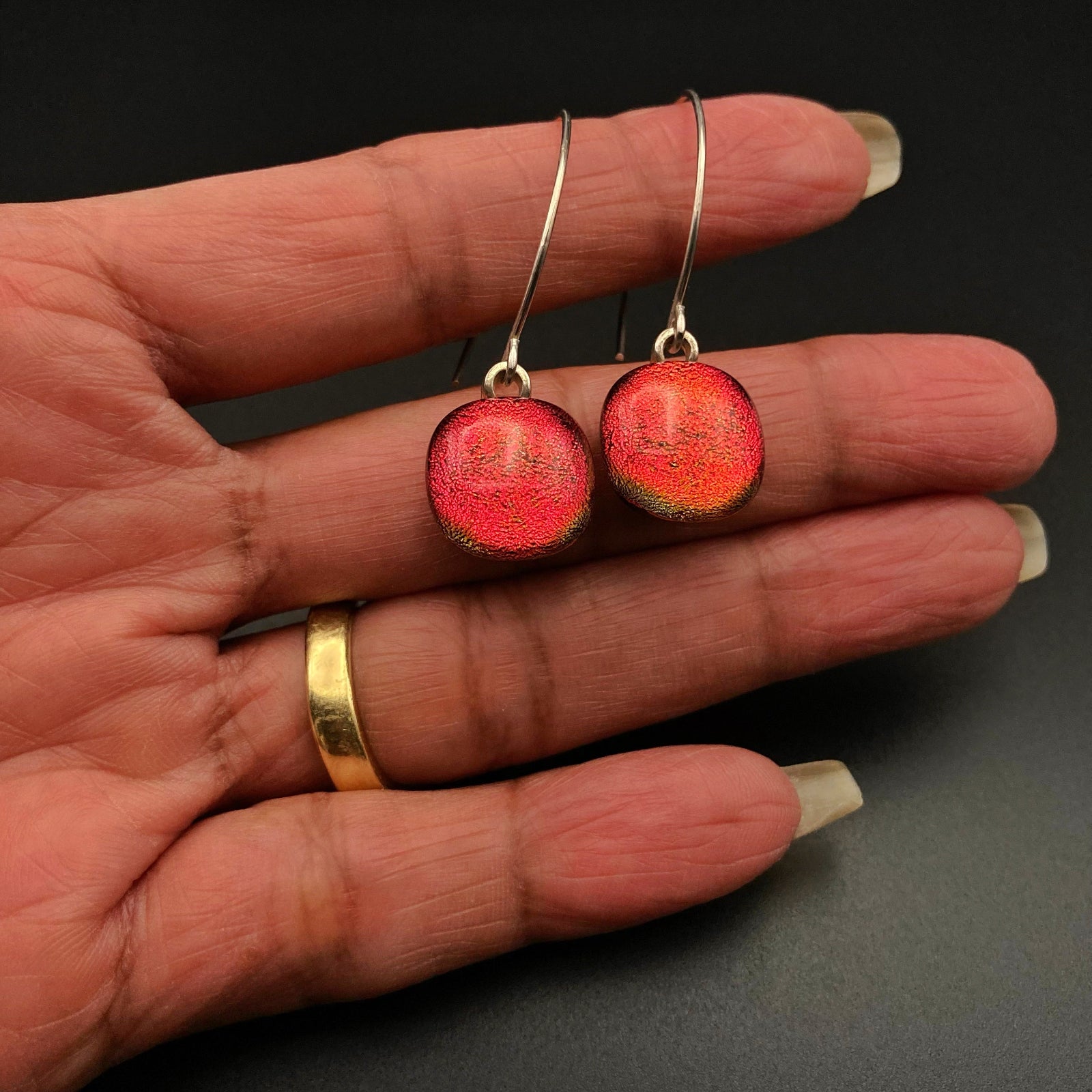 Hand holding pierced earrings with red dangles on silver ear wires, by 3D Glass Designs.