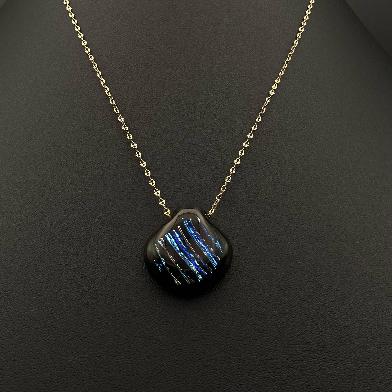 Pear-shaped fused glass pendant with gold chain against a black background, by 3D Glass Designs.