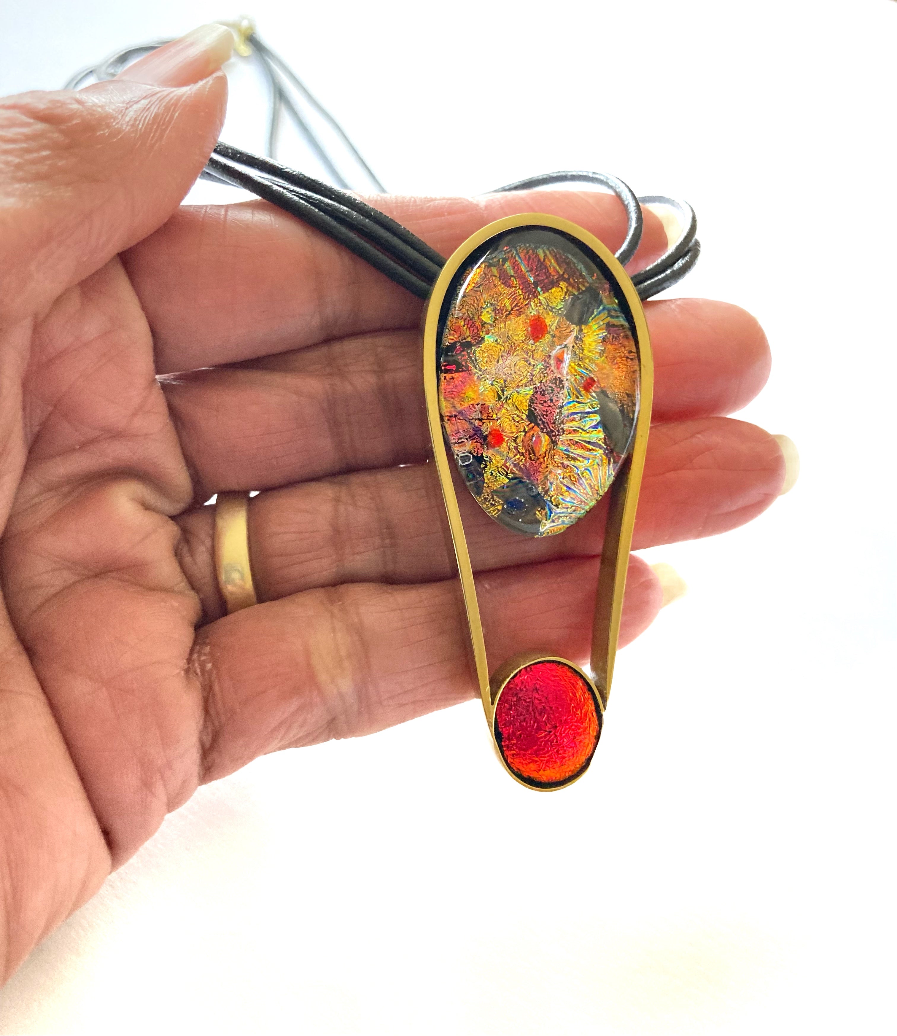 Hand holding contemporary fused glass pendant set in brass, by 3D Gass Designs.
