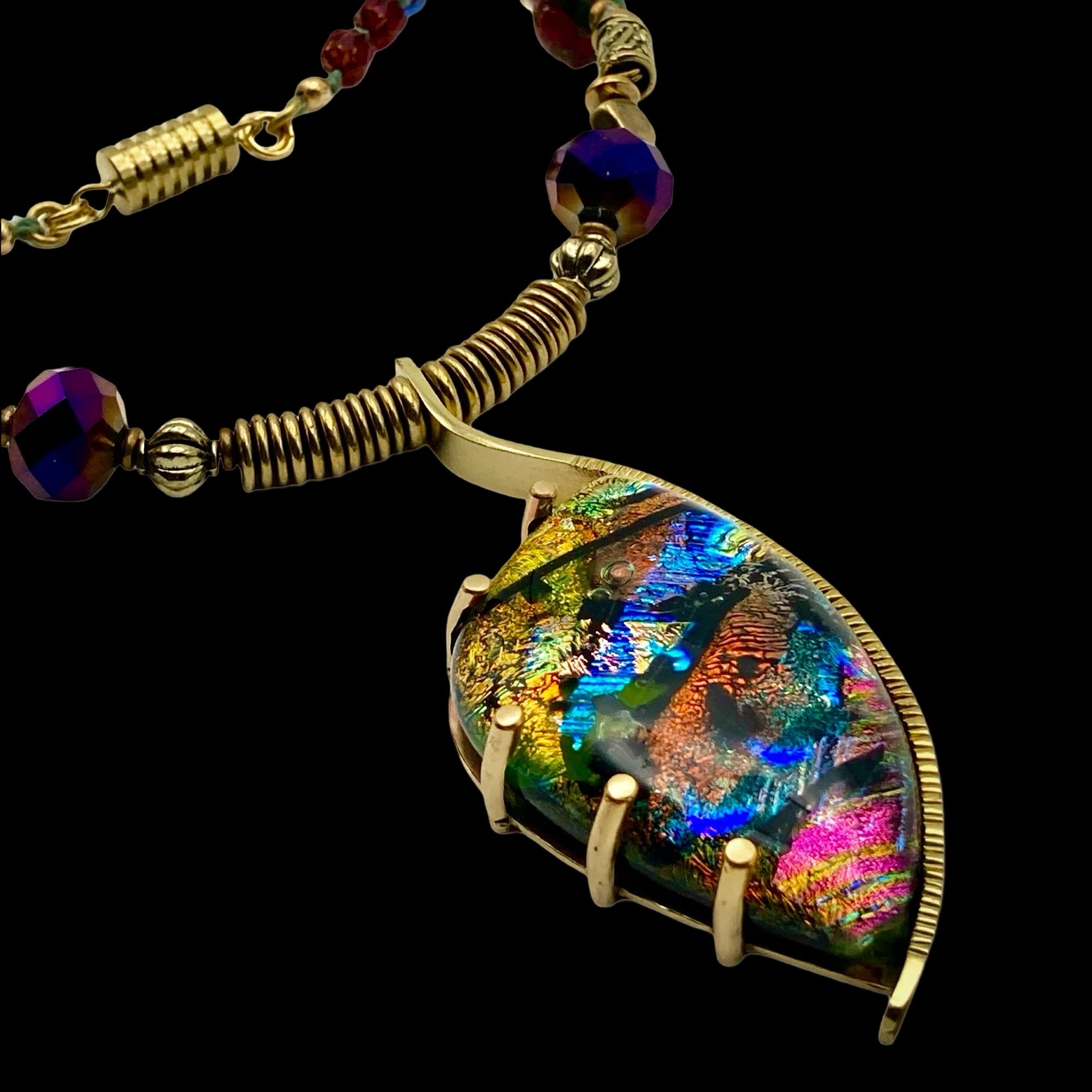 Dichroic glass set in a unique brass pendant, with prongs on left side and a textured bezel on the right side. Pendant is hung on a 29" long hand-knotted multicolor beaded necklace, by 3D Glass Designs.