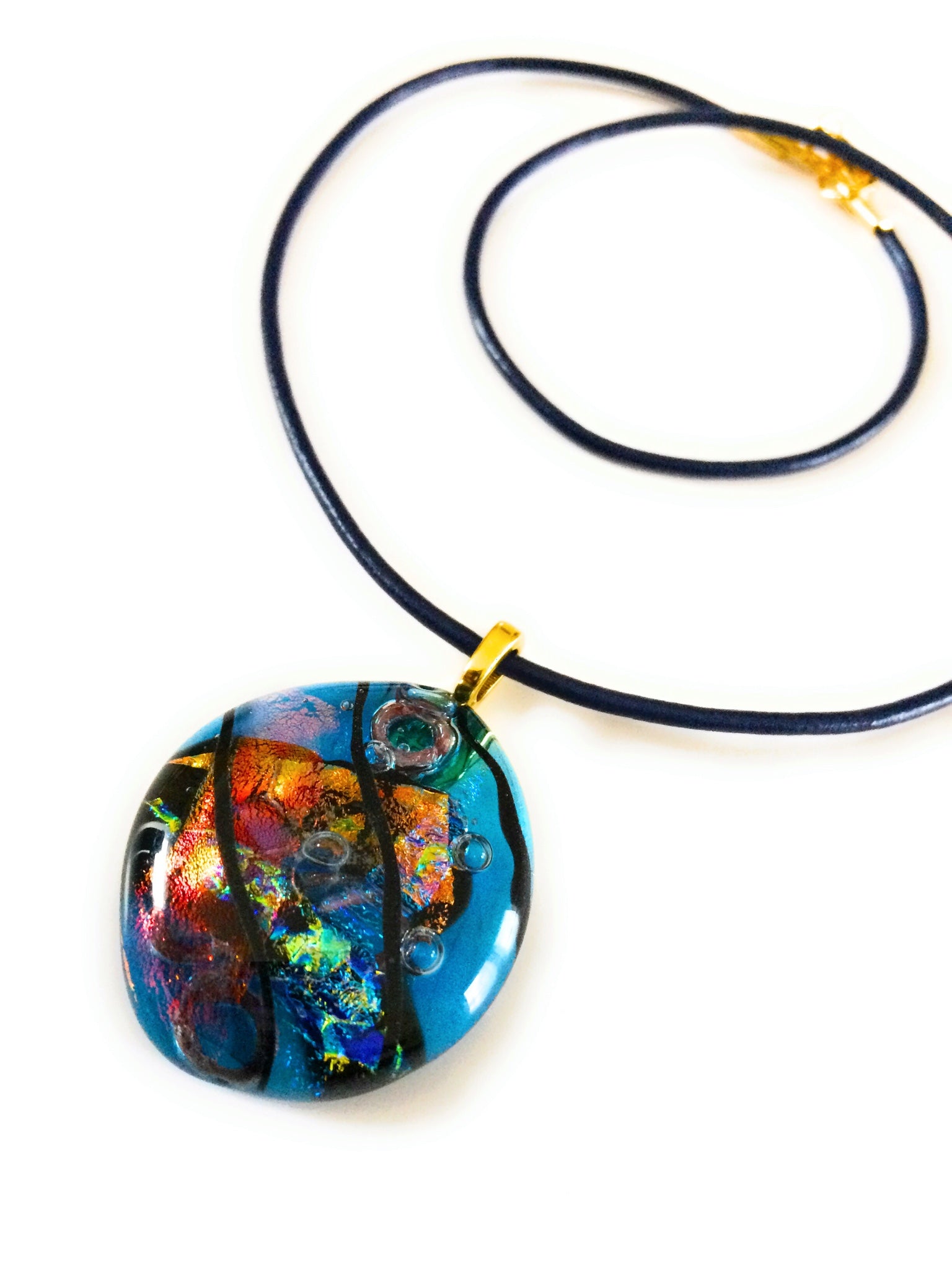 Fused glass pendant on a blue leather cord. Transparent blue glass with layers of red, rust, blue, green and purple dichroic glass and a copper squiggle design embedded in the glass. By 3D Glass Designs