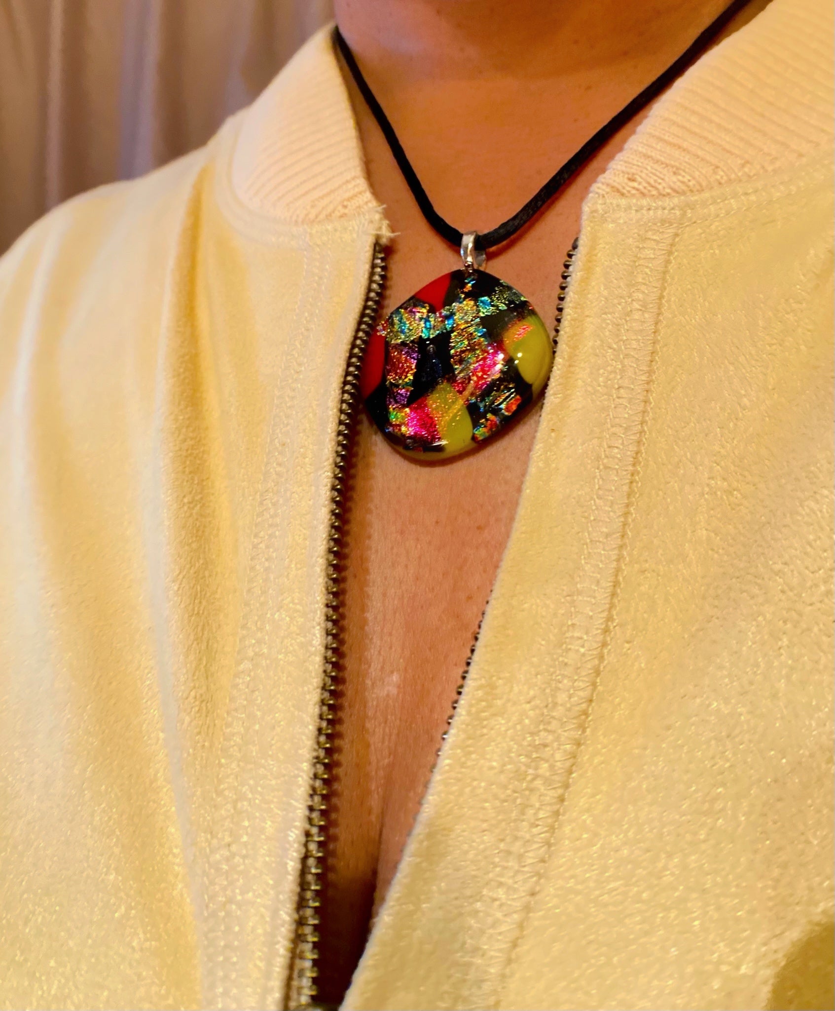 Model wearing multicolored fused glass pendant with a soft yellow zippered jacket, by 3D Glass Designs.
