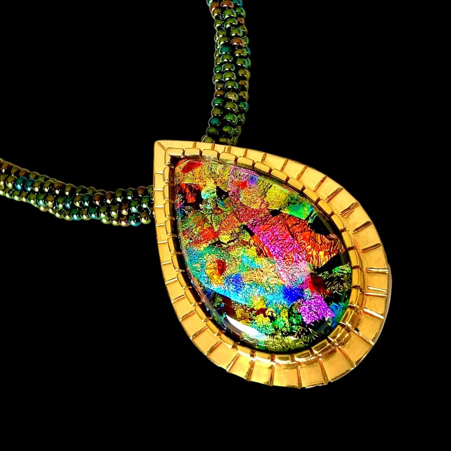Handcrafted multicolor teardrop shaped dichroic glass, set in a custom-made brass setting, with a handmade seed bead and leather necklace. By 3D Glass Designs.