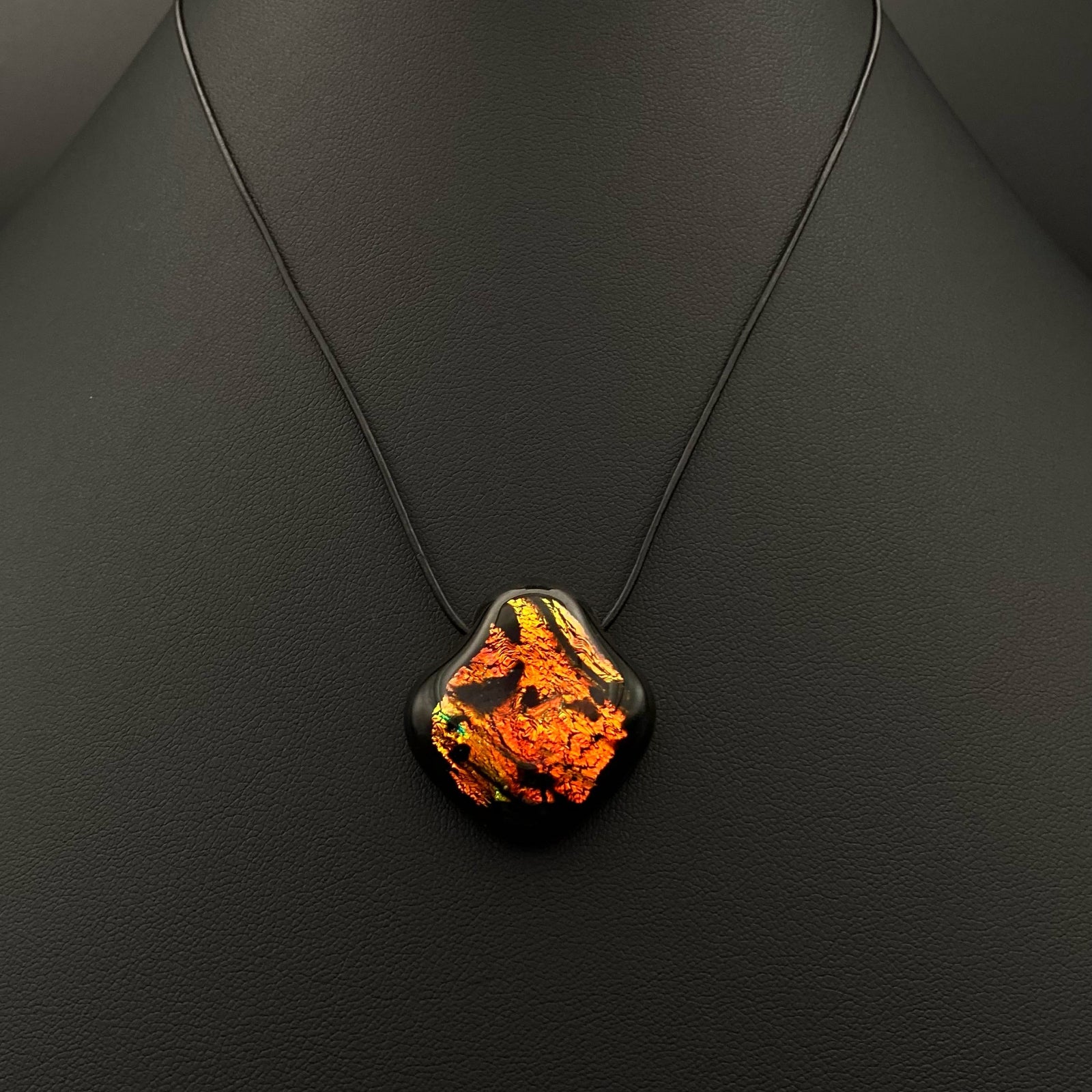 Orange and black pendant on a black leather cord against a black background, by 3D Glass Designs.