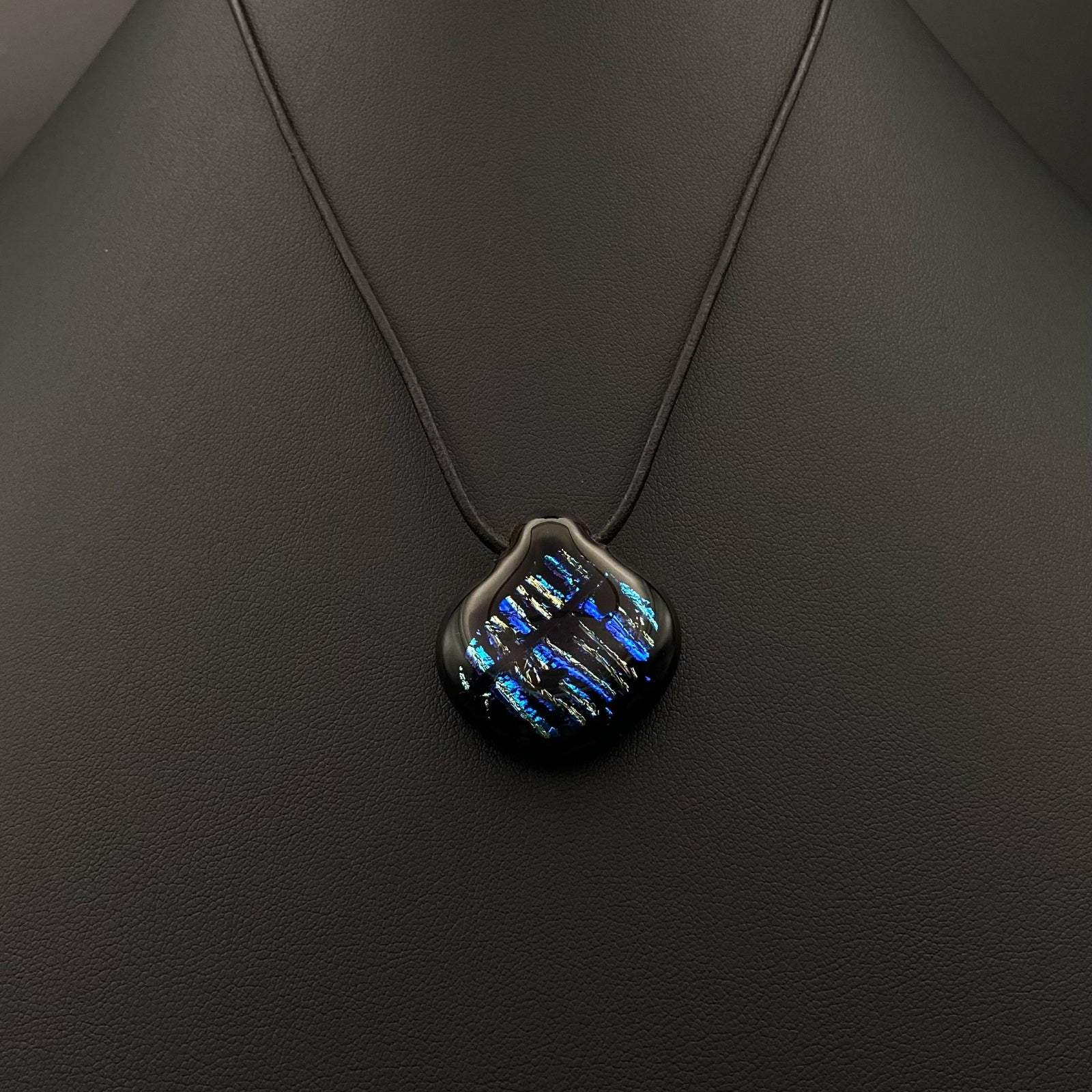 Pear-shaped dichroic glass pendant with blue stripes on a black leather cord against a black background, by 3D Glass Designs.