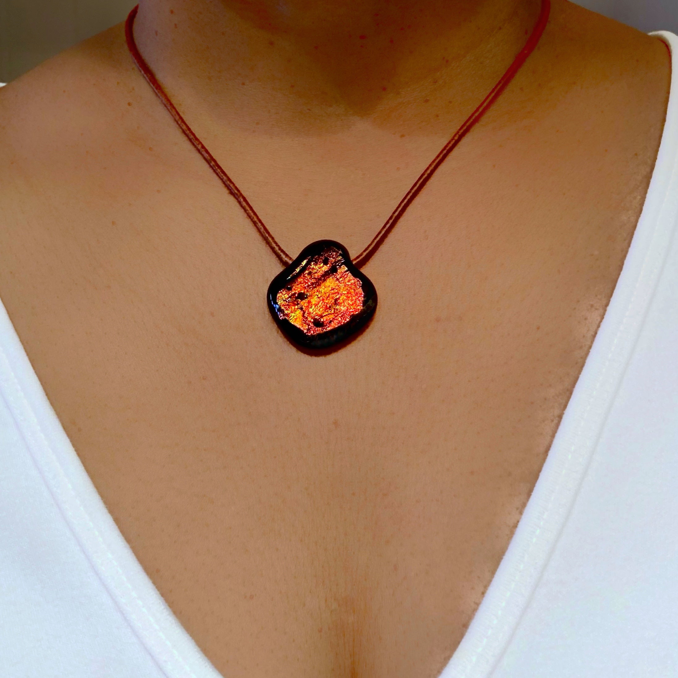 Model wearing white shirt and reddish color fused glass pendant on a brown leather cord, by 3D Glass Designs.