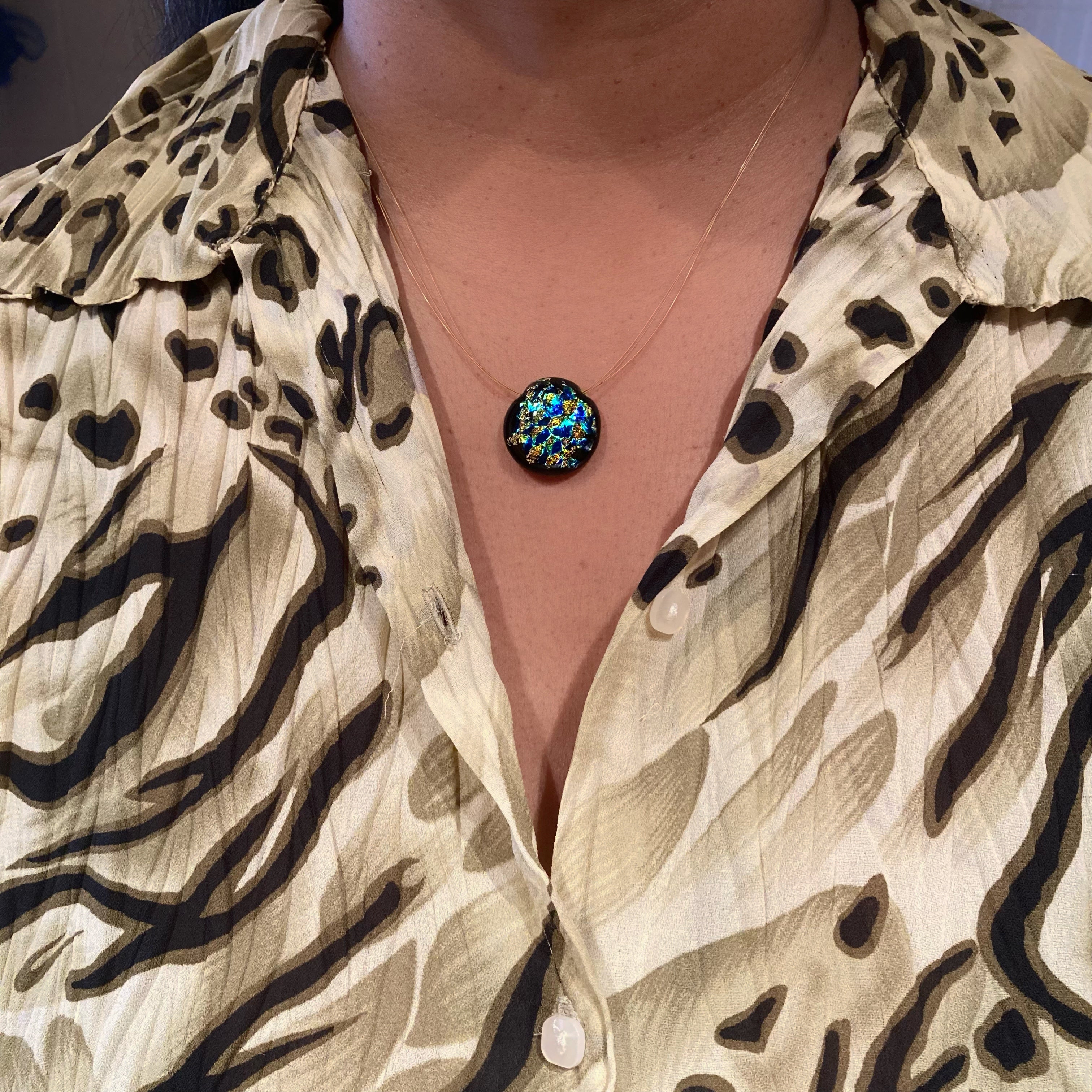 Model wearing small round glass pendant, in blue green and gold, floating on three gold cords, by 3D Glass Designs.