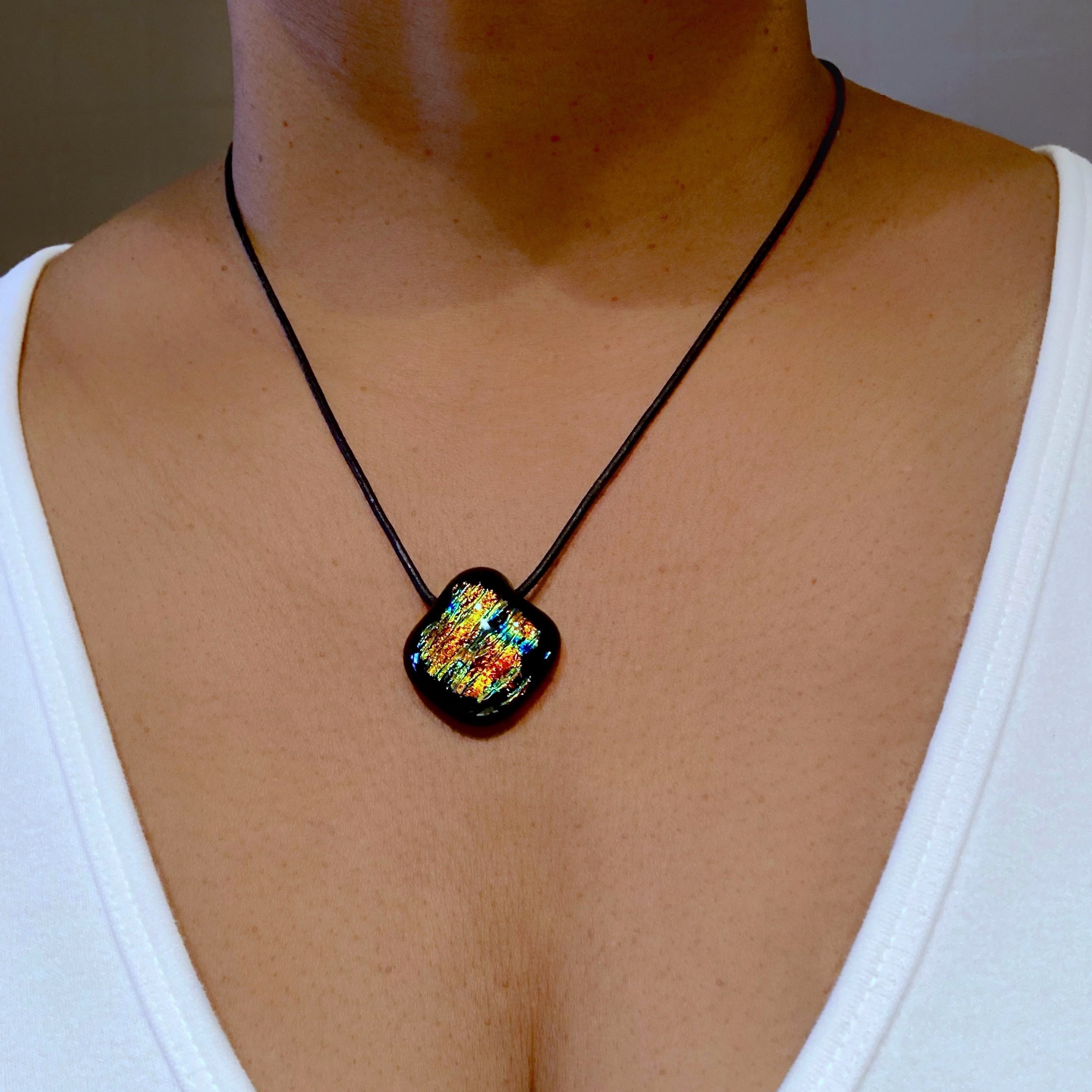 Model wearing a white shirt and a colorful glass pendant on a black leather cord, by 3D Glass Designs.