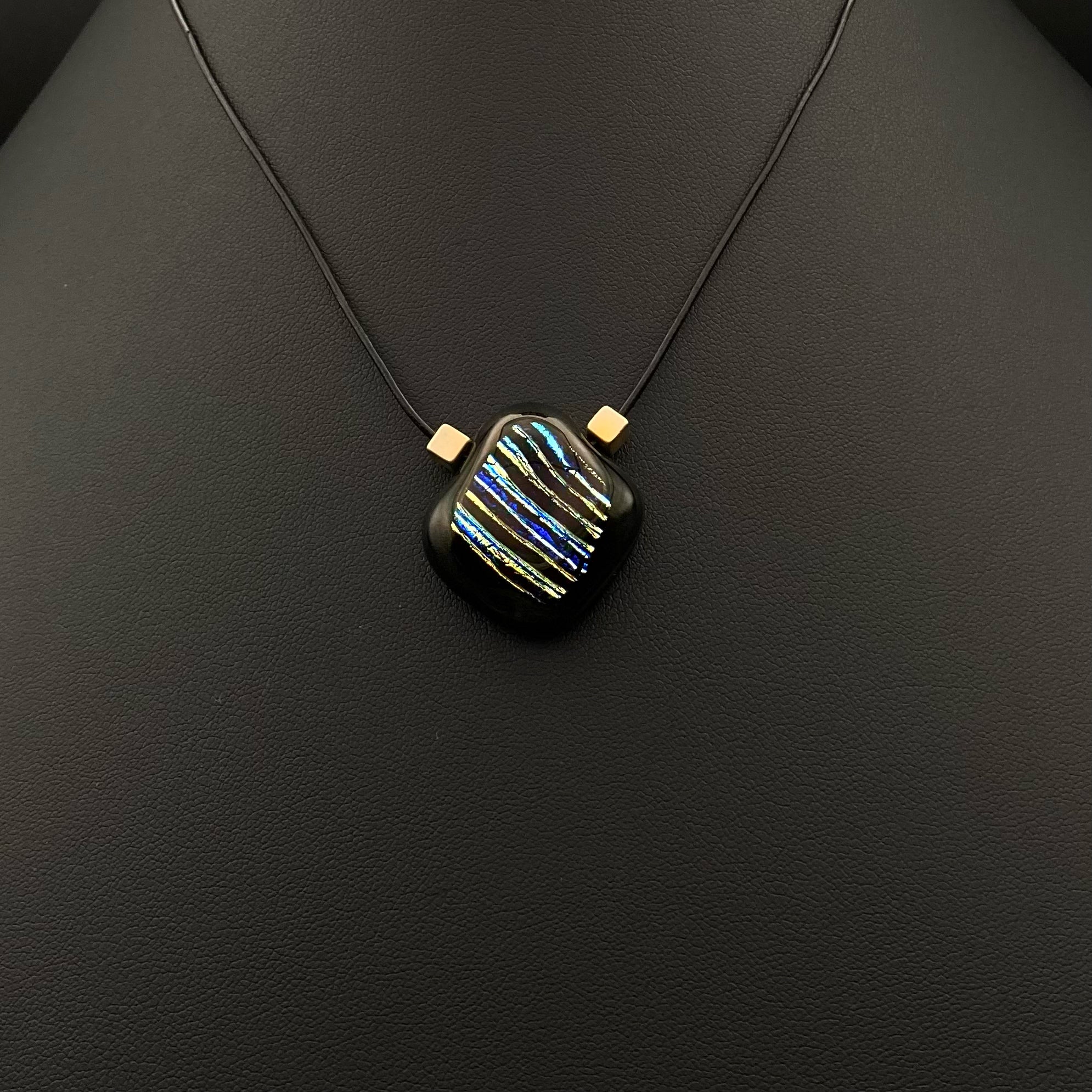 Small glass pendant with blue and silver stripes and two cube beads on a thin black leather cord, by 3D Glass Designs.