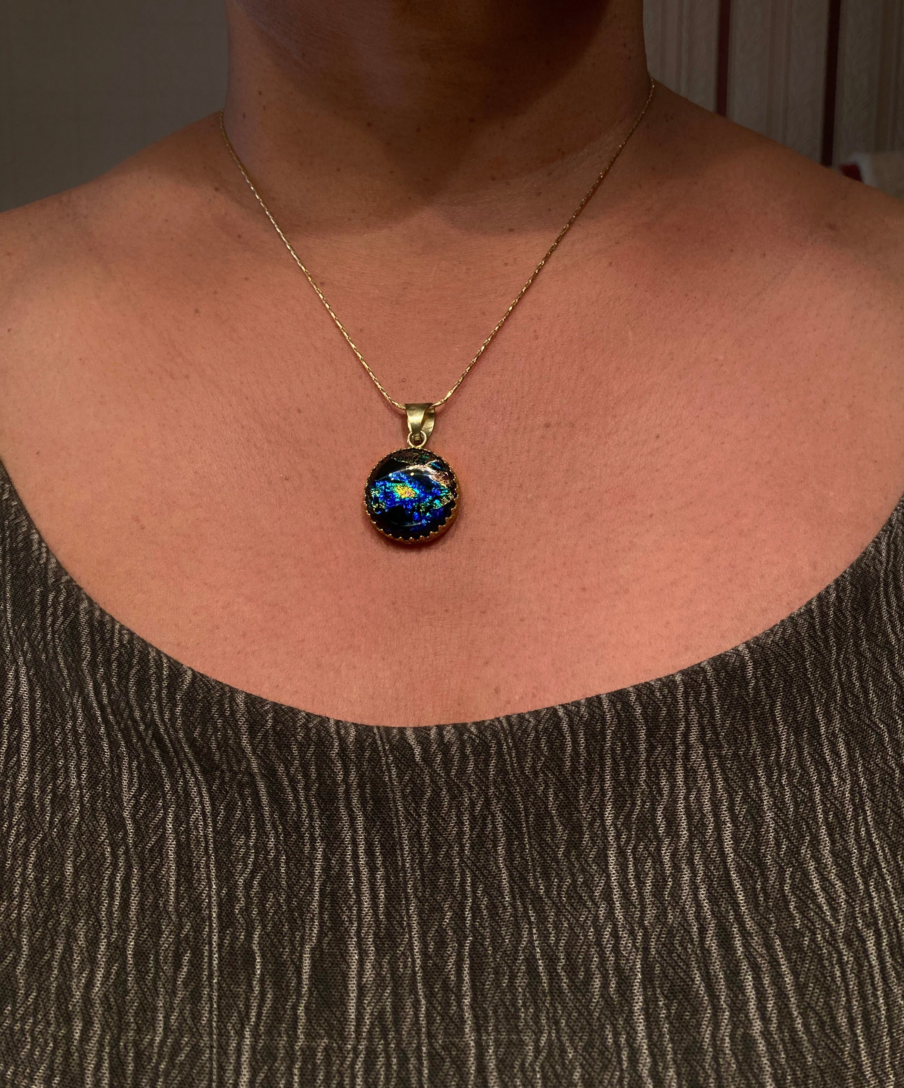 Model wearing a small, handcrafted dichroic glass pendant in brass setting.