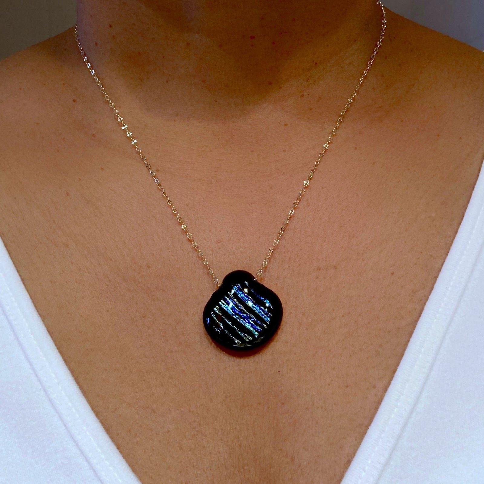 Model wearing delicate gold chain with dichroic glass pendant, 3D Glass Designs.