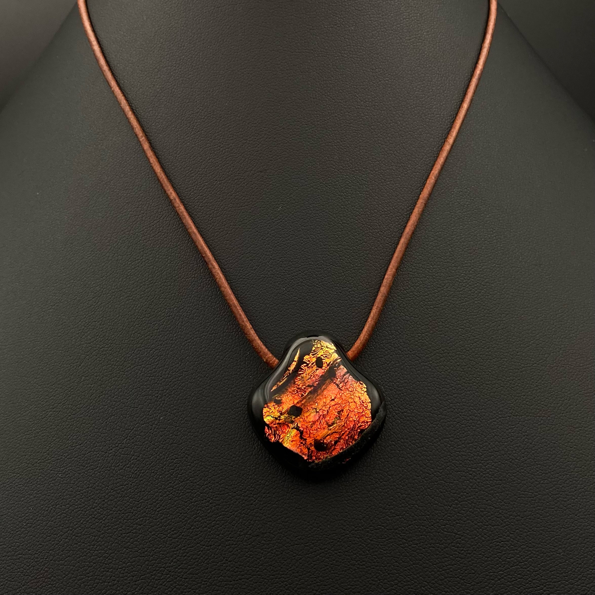 Dichroic fused glass pendant on a brown leather cord against a black leather background, by 3D Glass Designs.