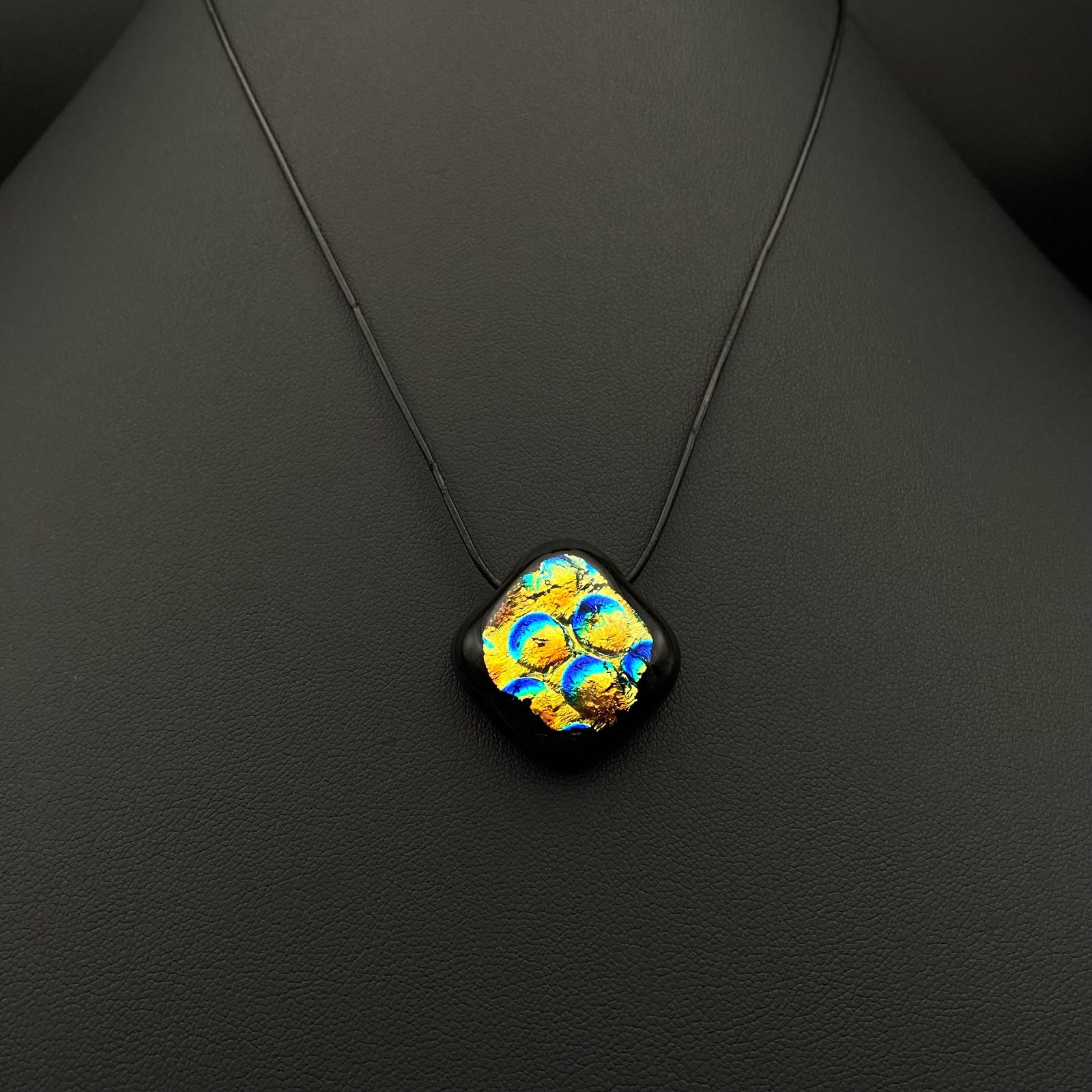 Small blue, gold and black glass pendant against a black leather background, by 3D Glass Designs.
