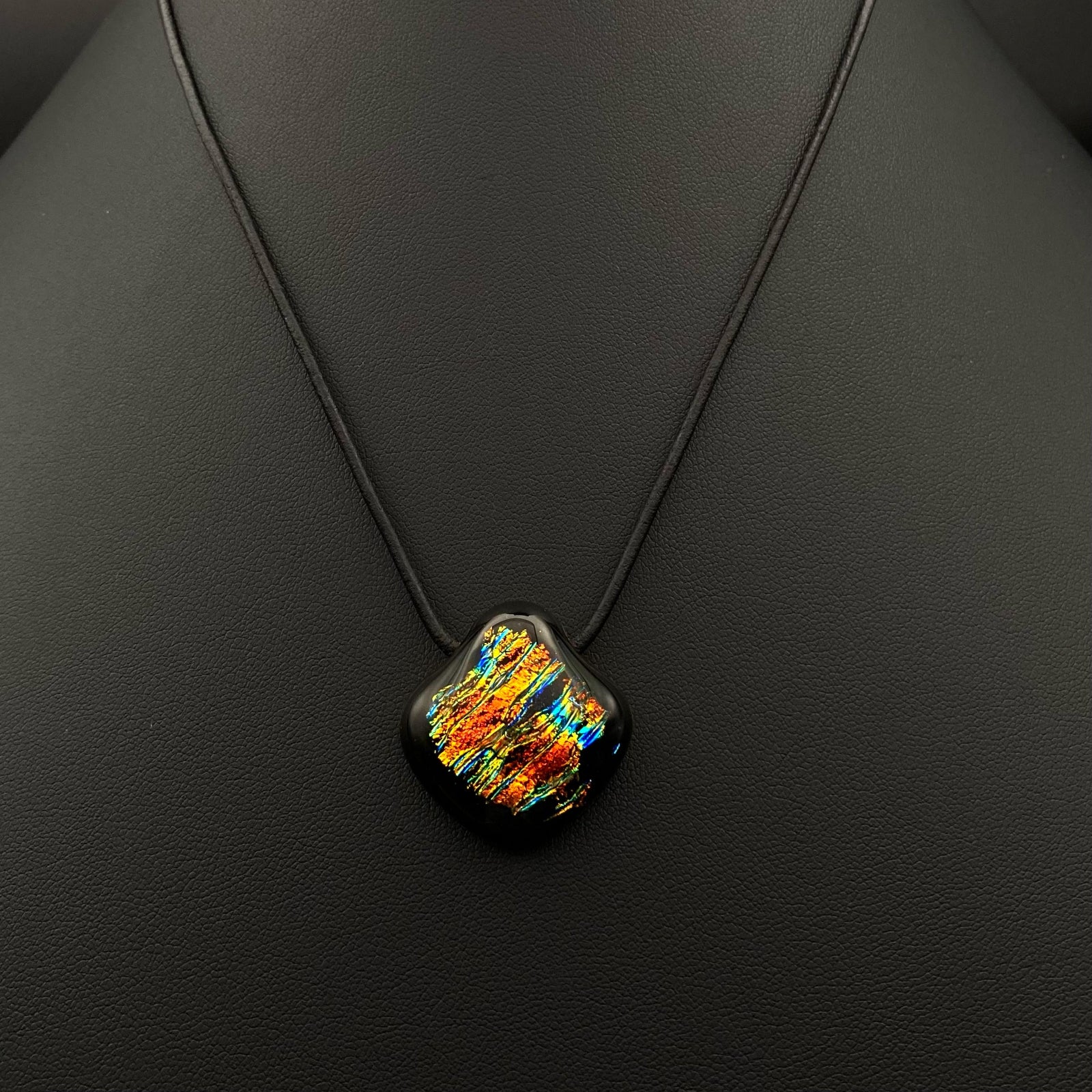 Colorful glass pendant on a black leather cord against a black background, by 3D Glass Designs.