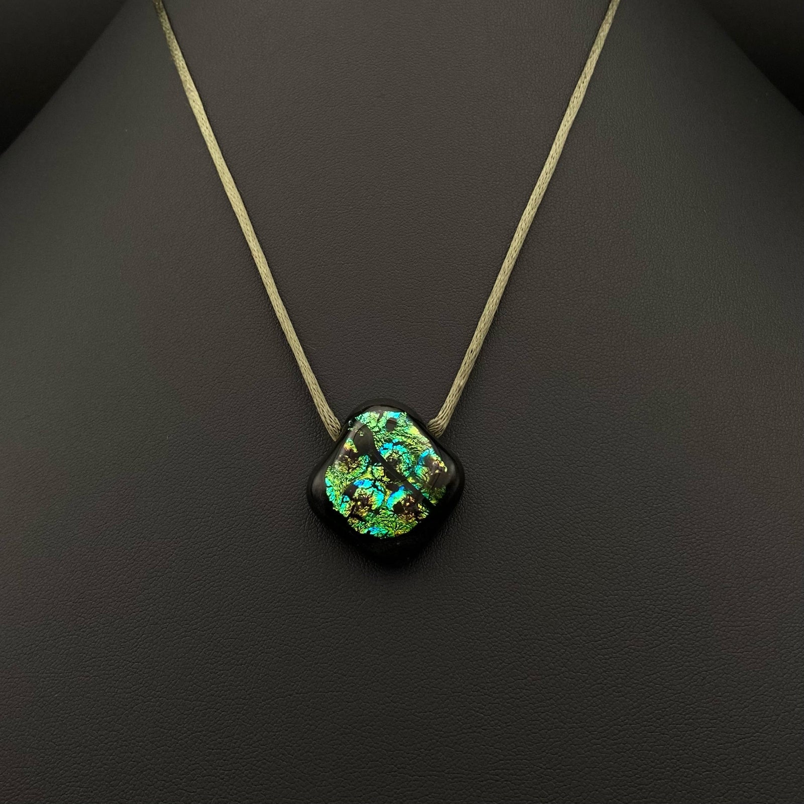 Green glass pendant on an olive-green satin cord against a black background, by 3D Glass Designs.