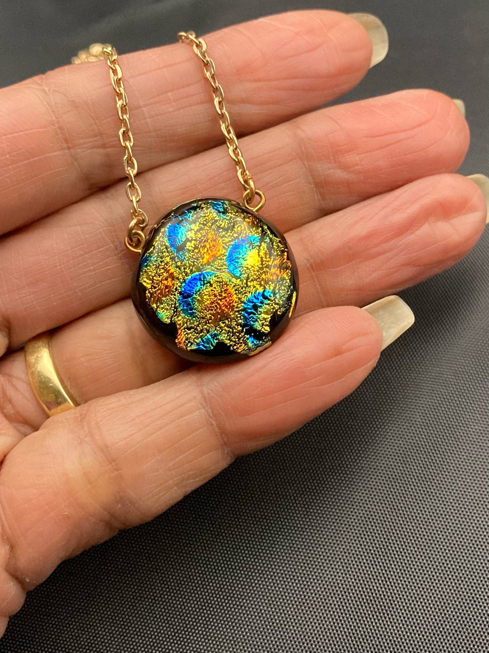 Hand holding small round colorful glass pendant on a gold chain, by 3D Glass Designs.