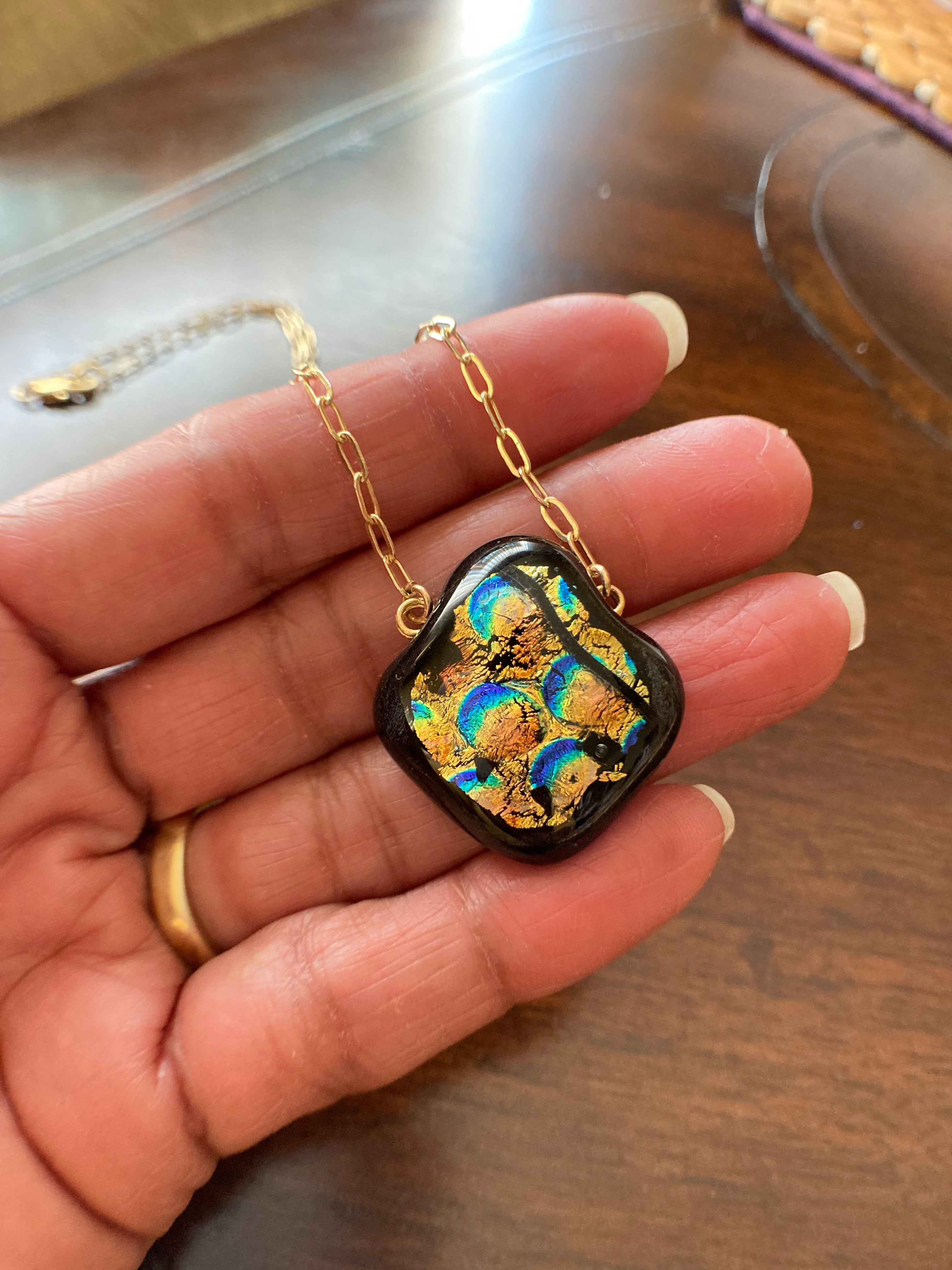 Hand holding fused glass pendant against a wooden table, by 3D Glass Designs.