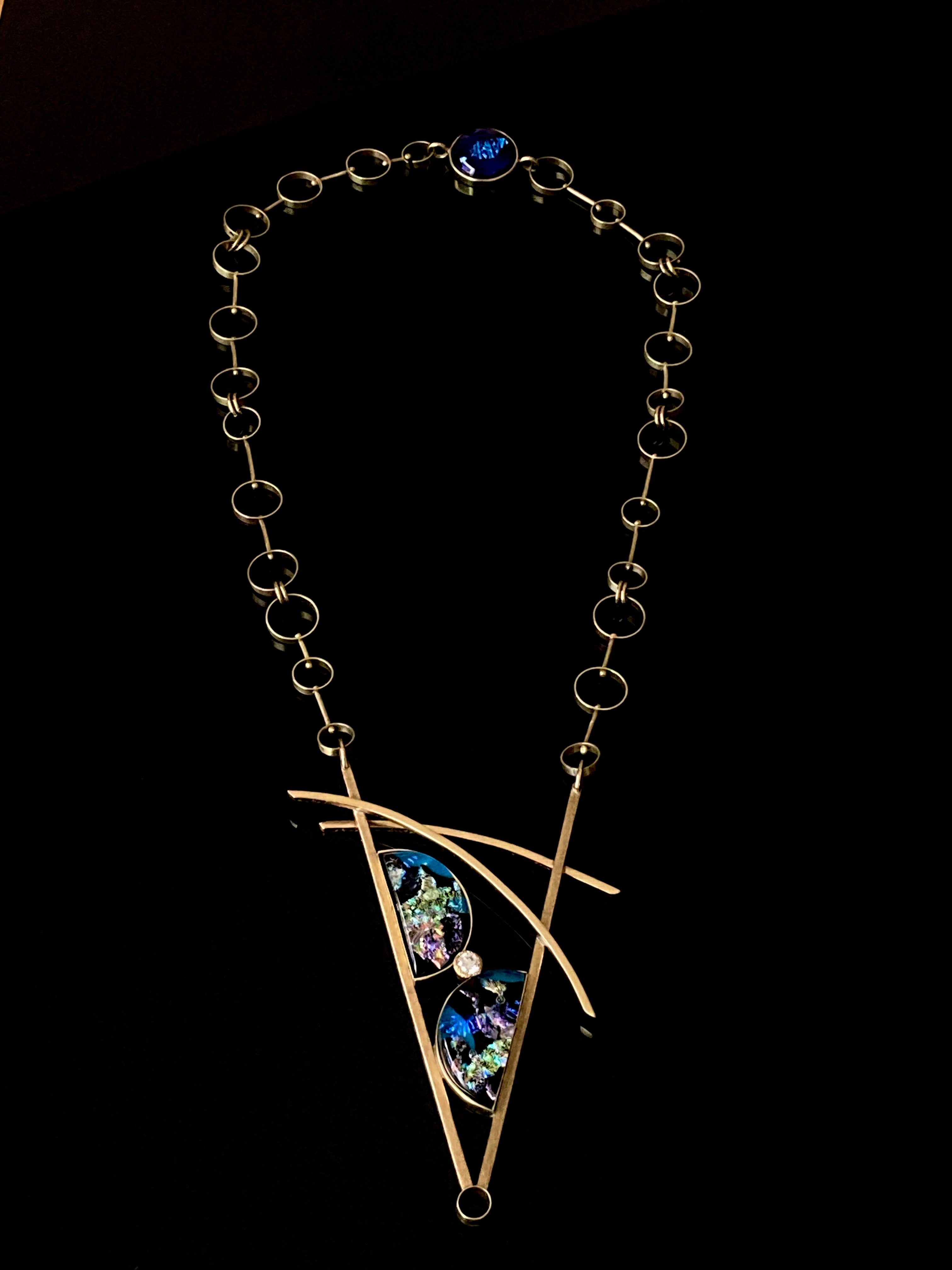 Geometric inspired brass pendant with teal fused glass in semi-circles and CZ, framed in a V with two slightly curved arch's above. Necklace made of various sized circles linked together, by 3D Glass Designs.